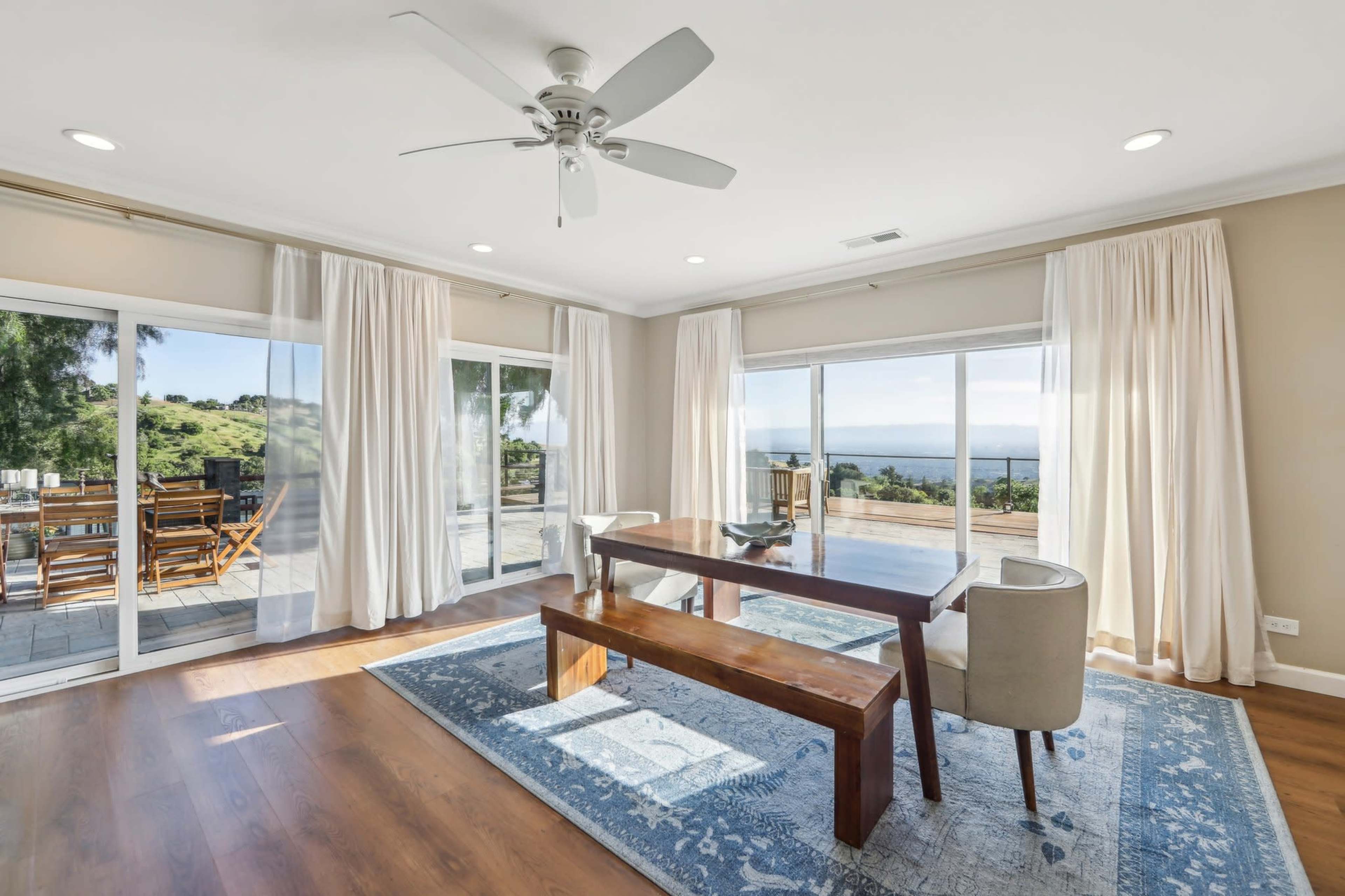 A dining area features a wooden table and chairs, with large windows offering a view of the outdoors.