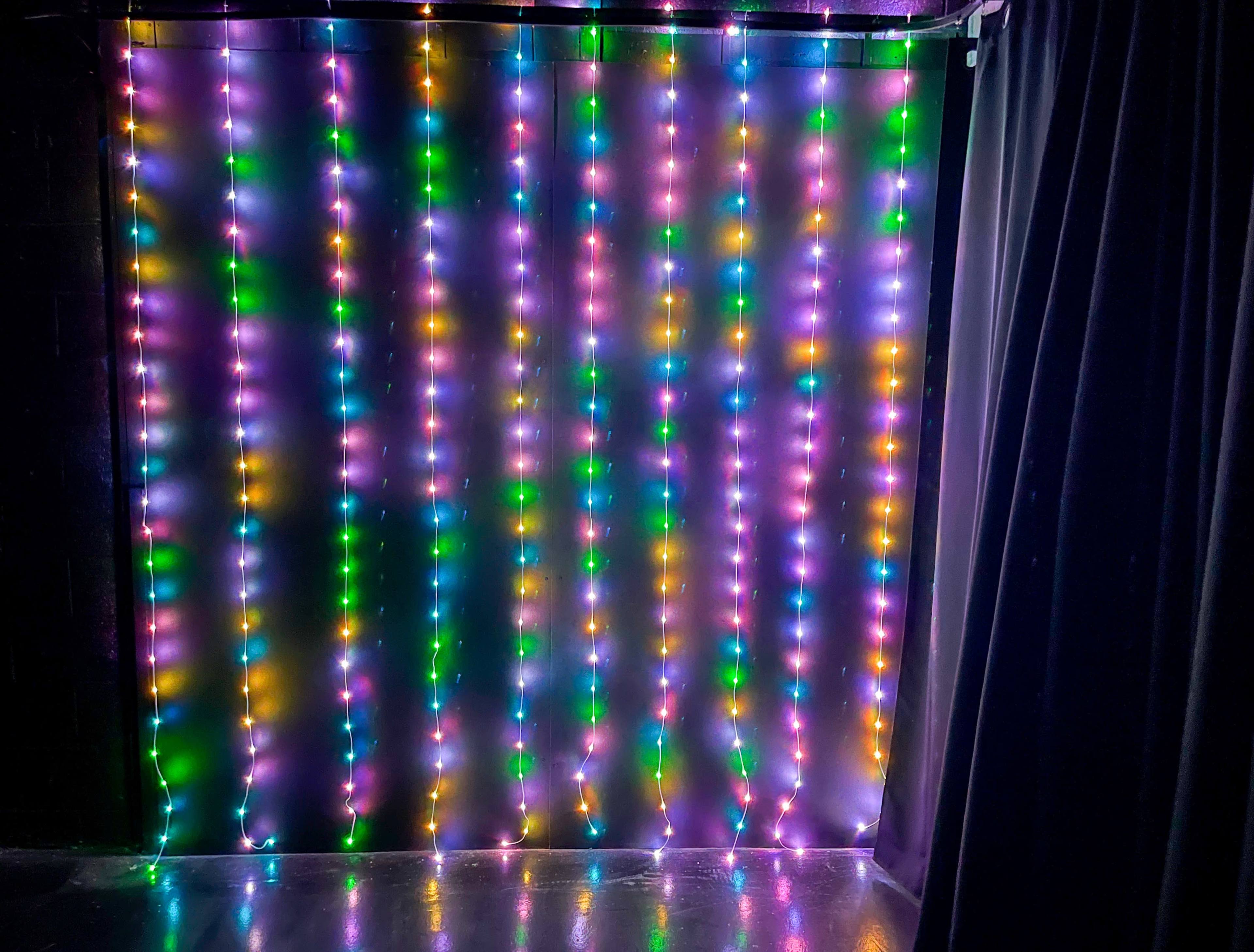 A wall covered with vertically hanging string lights in various colors.