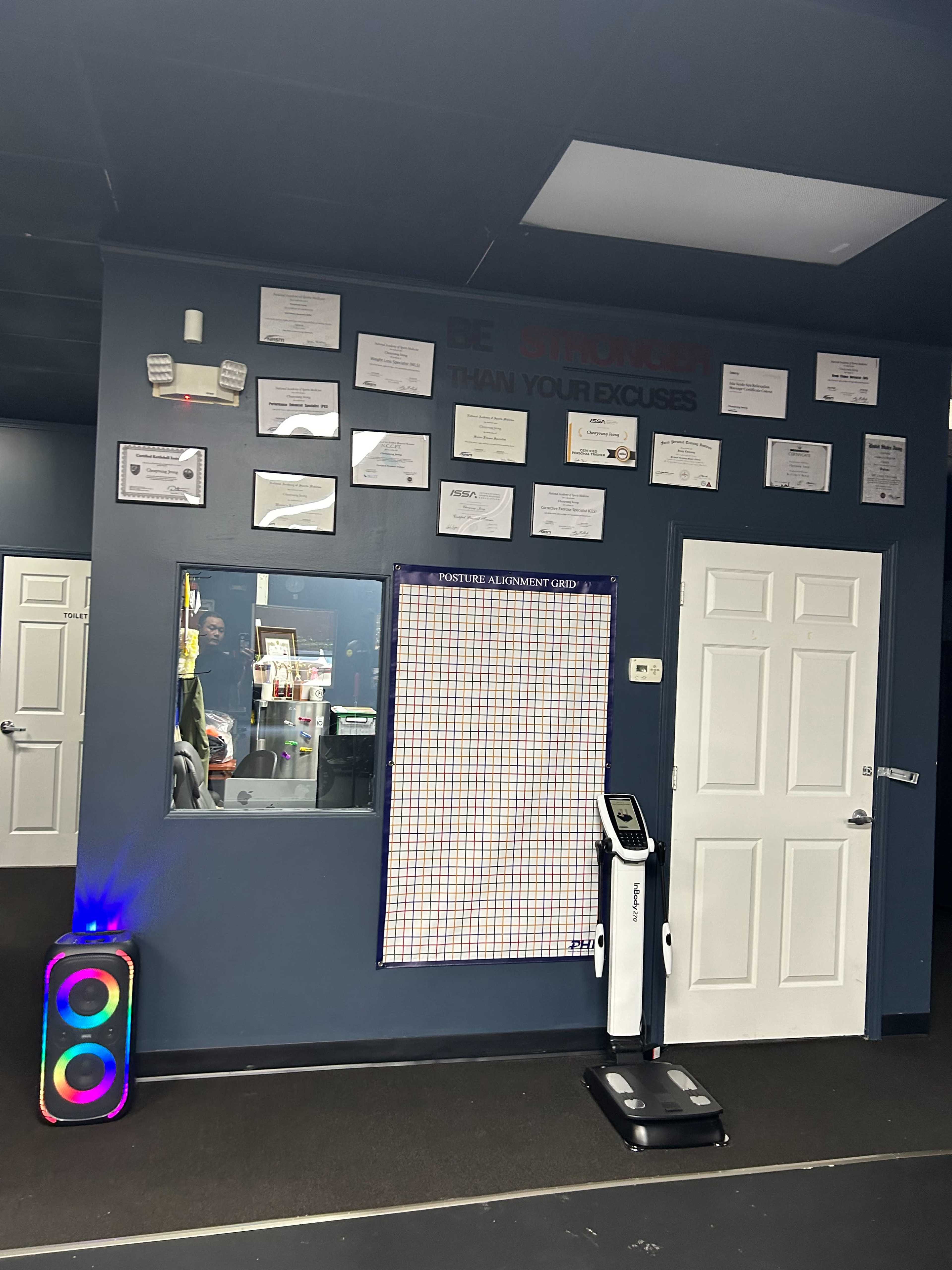 A blue wall decorated with certificates and a grid chart alongside a window and two doors in a fitness studio.