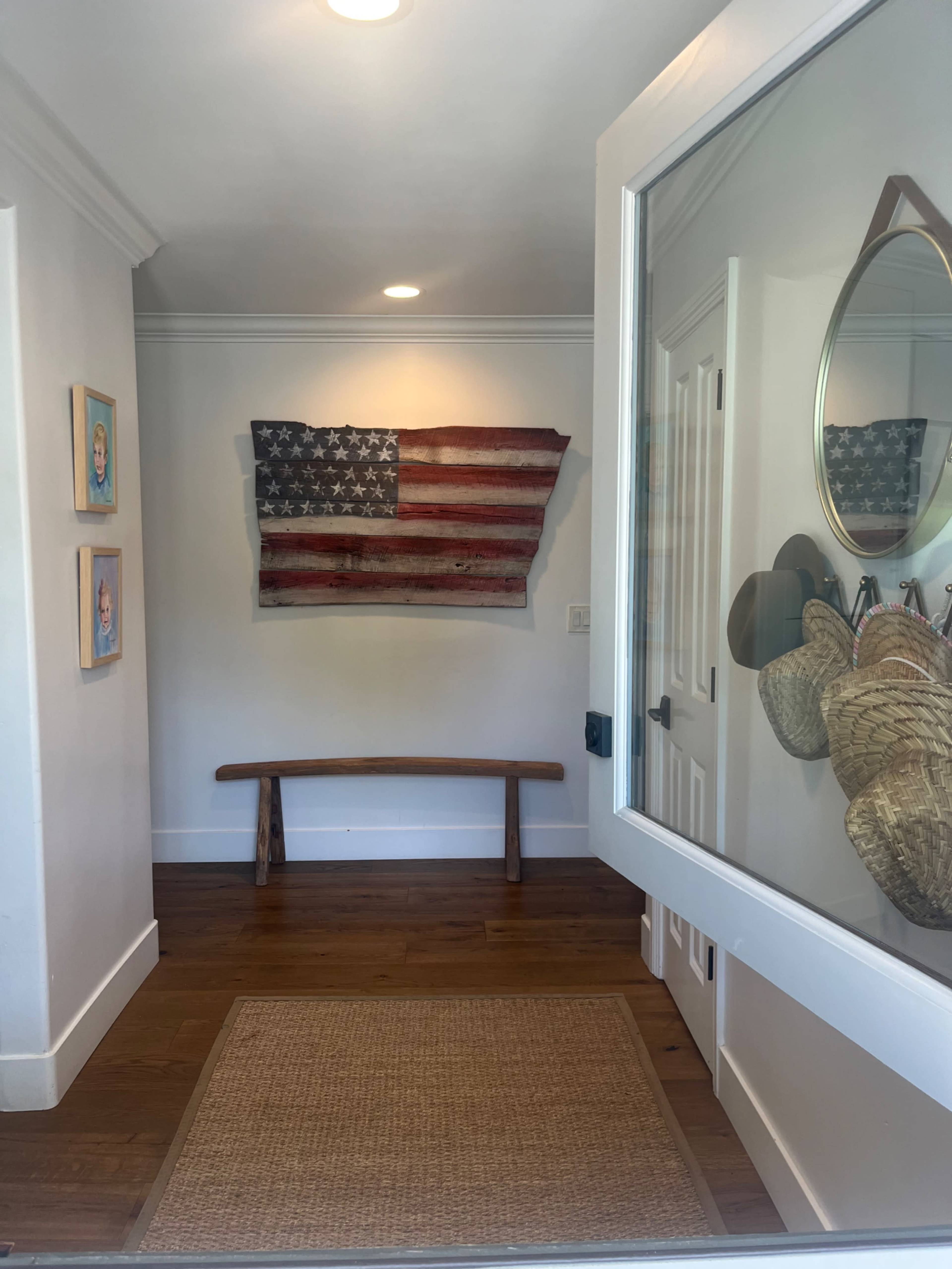 An entryway with a wooden bench, a jute rug, and a distressed American flag mounted on the wall.