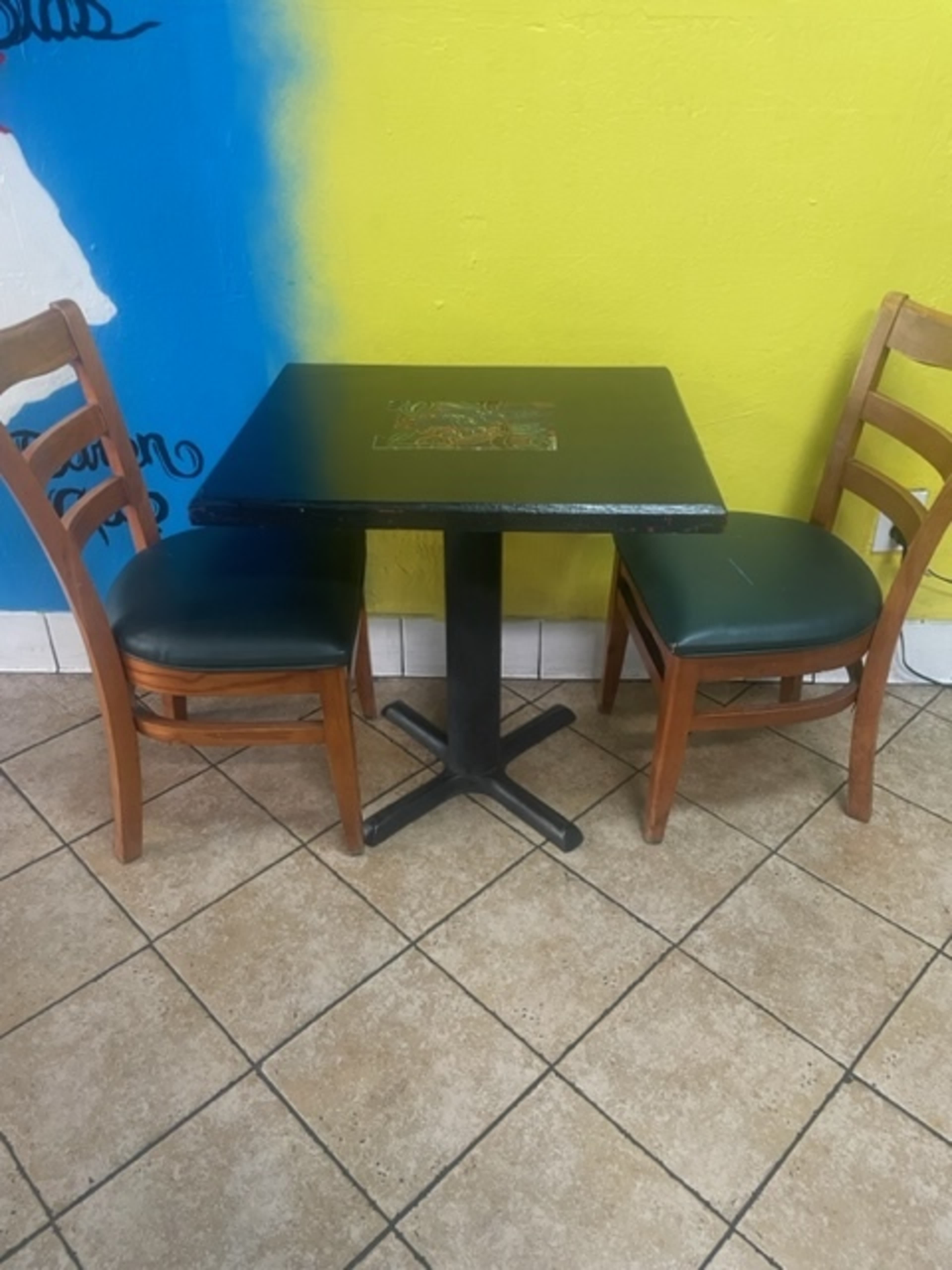 A small, black table stands between two wooden chairs in a brightly colored room with a yellow wall.