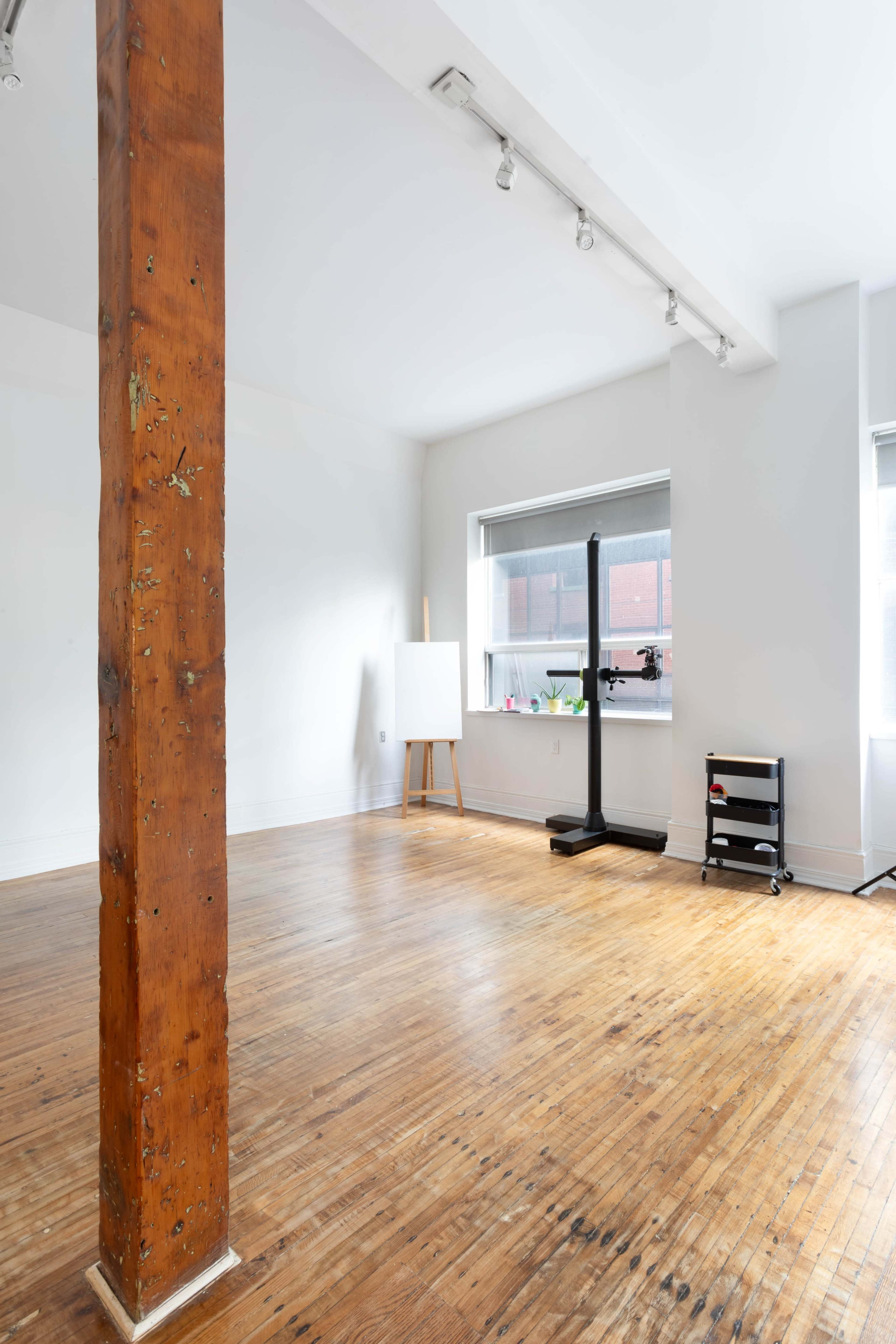 A spacious, empty room with hardwood floors, a wooden support pillar, a blank easel, and a black stand in the corner.