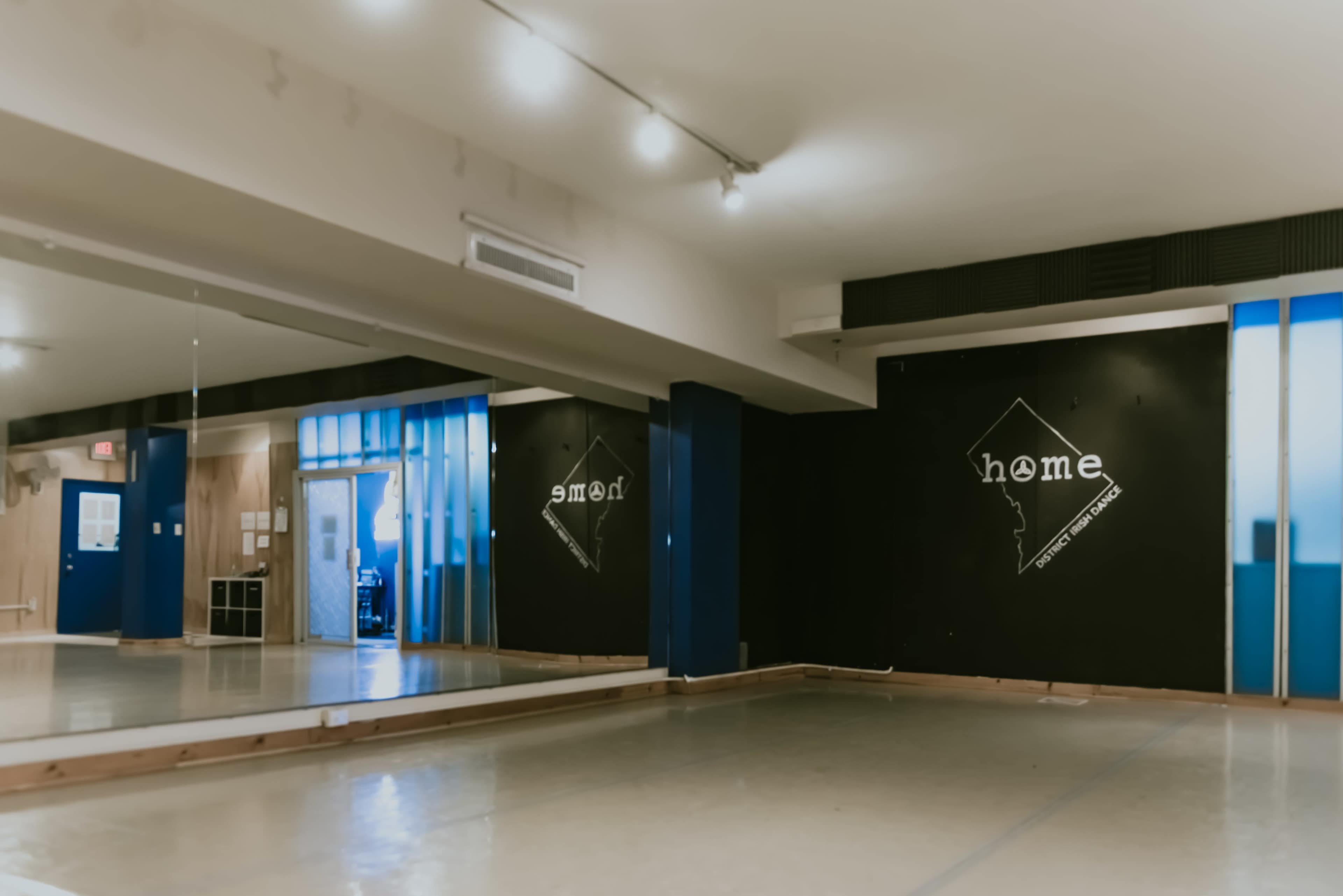 A spacious dance studio with mirrored walls, wooden flooring, and two black walls featuring the words "smile" and "home."