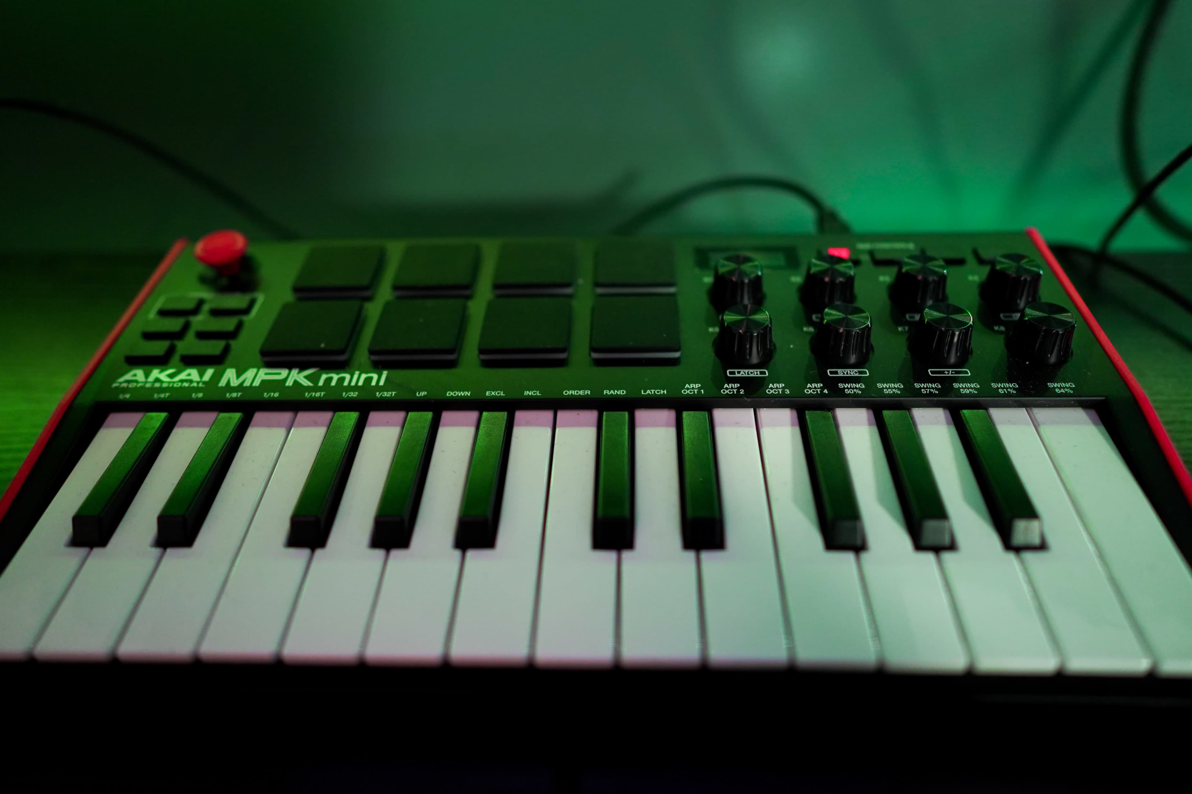 The image shows an Akai MPK Mini MIDI controller with keys and pads, placed on a dark surface illuminated by green light.