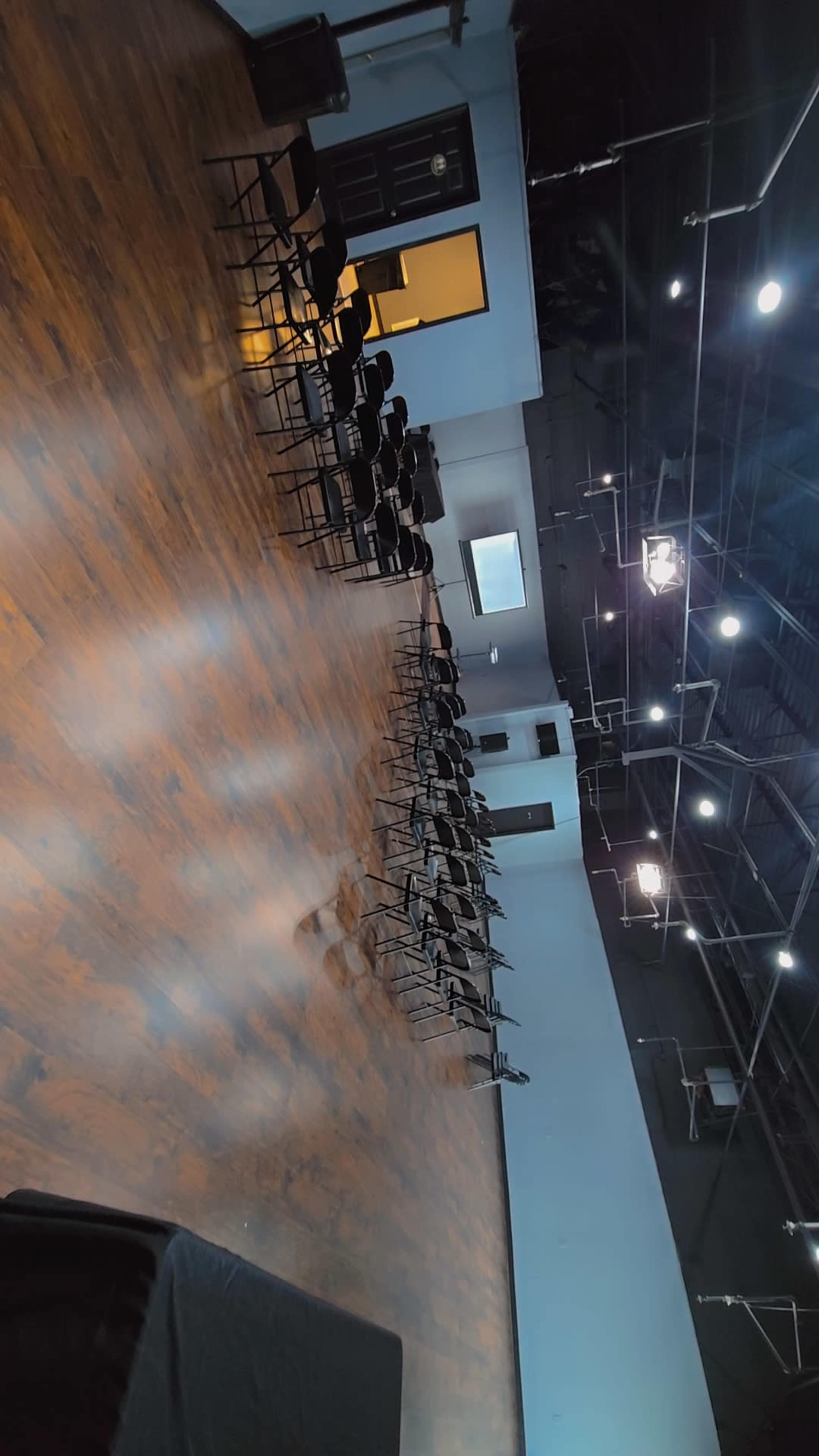 The image shows a spacious room with a polished wooden floor and neatly arranged black chairs facing a wall with a doorway.