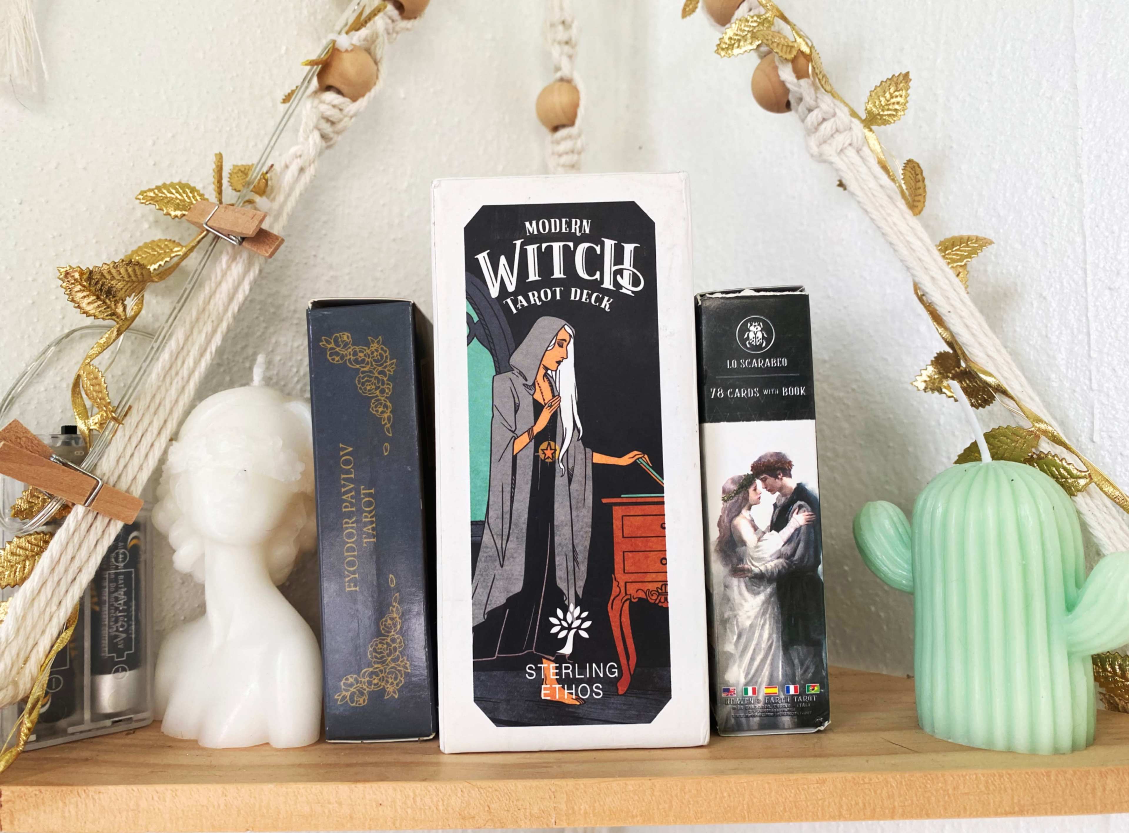 A wooden shelf displays a Modern Witch tarot deck, flanked by boxes of other tarot decks and decorative items.