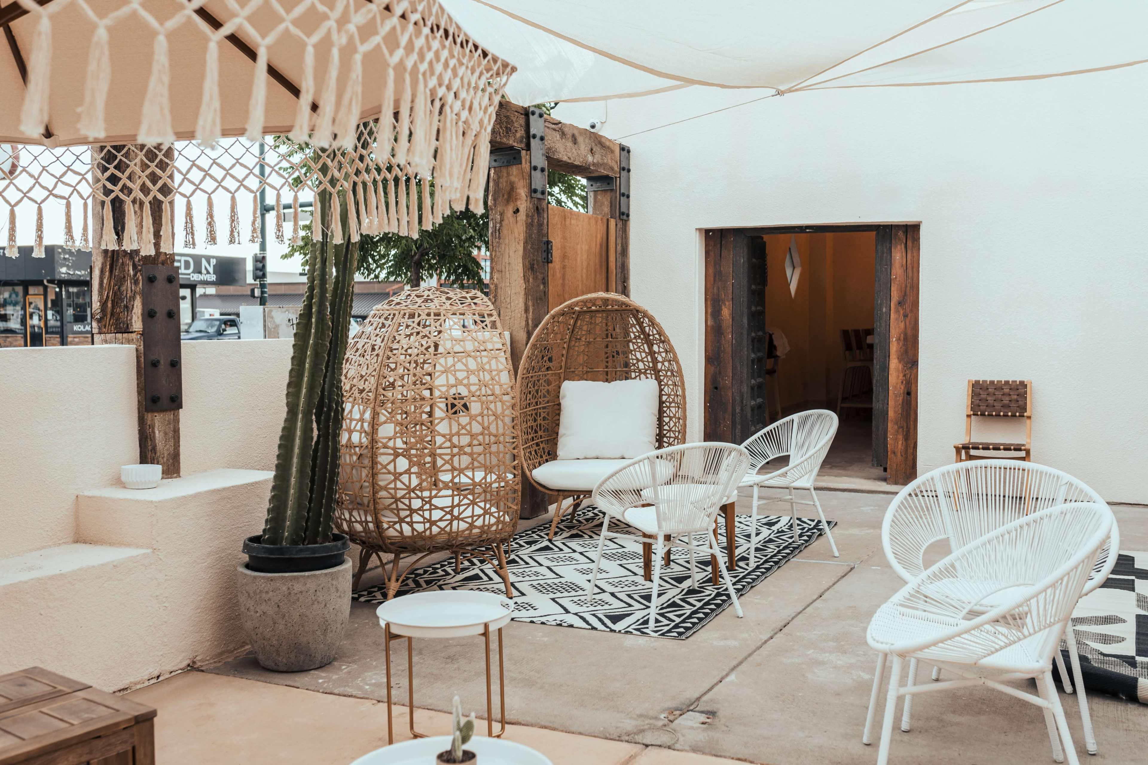 A cozy outdoor seating area featuring woven chairs, a patterned rug, and potted plants under a canopy.