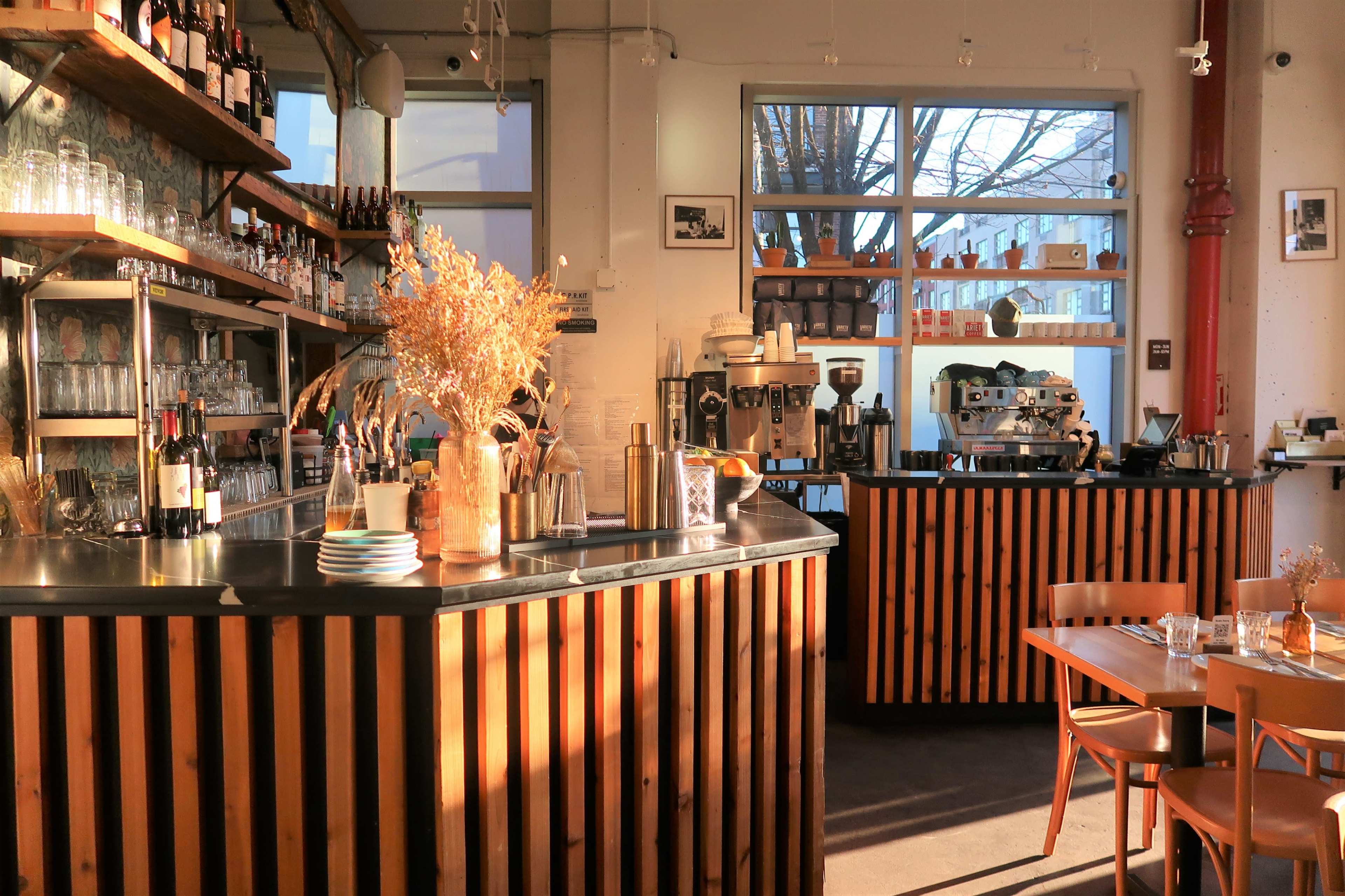 A modern café interior with wooden cabinetry, large windows allowing natural light, and a coffee bar featuring an espresso machine.
