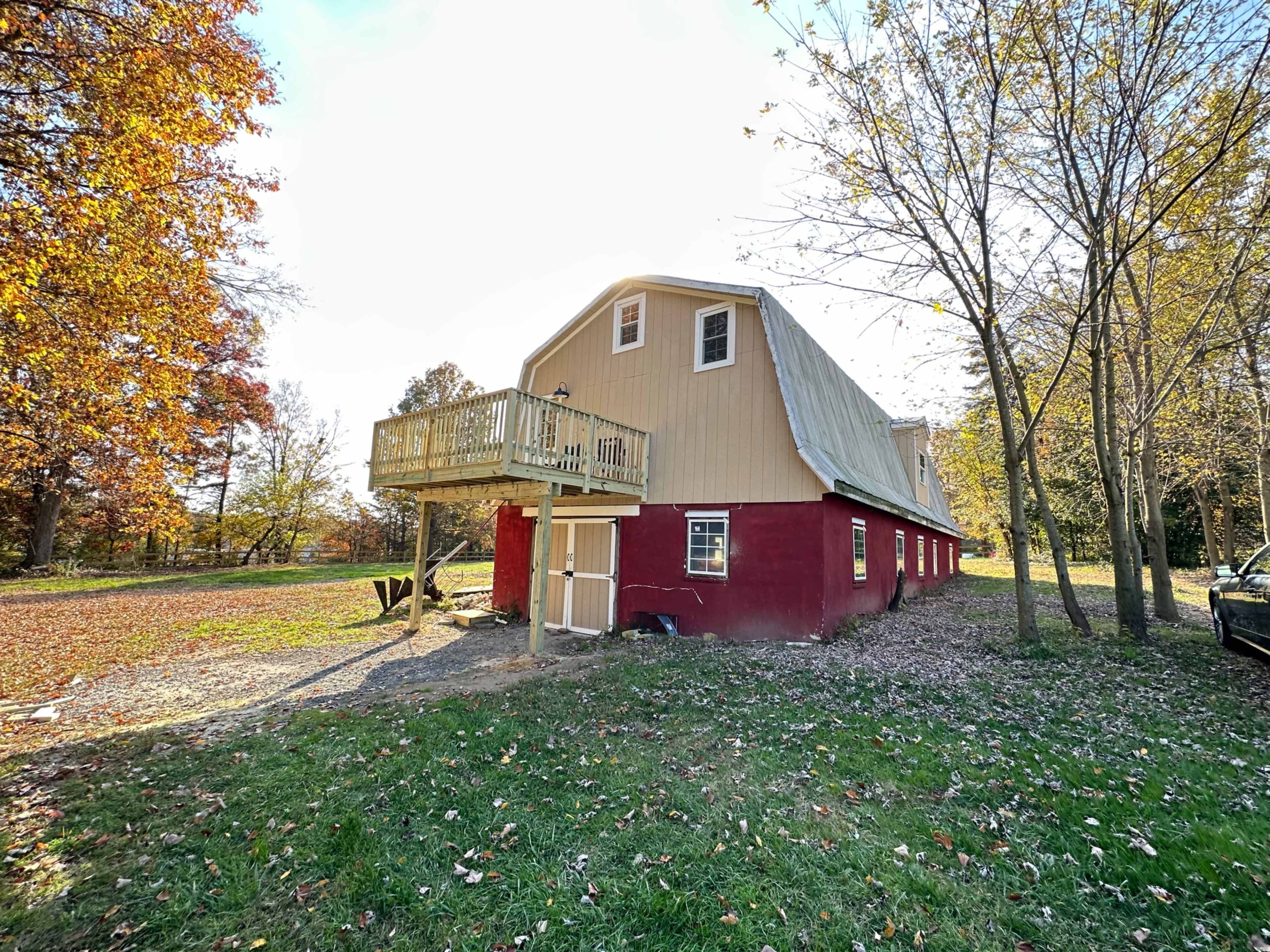 A two-toned barn with a balcony, surrounded by trees and fallen leaves on the ground.