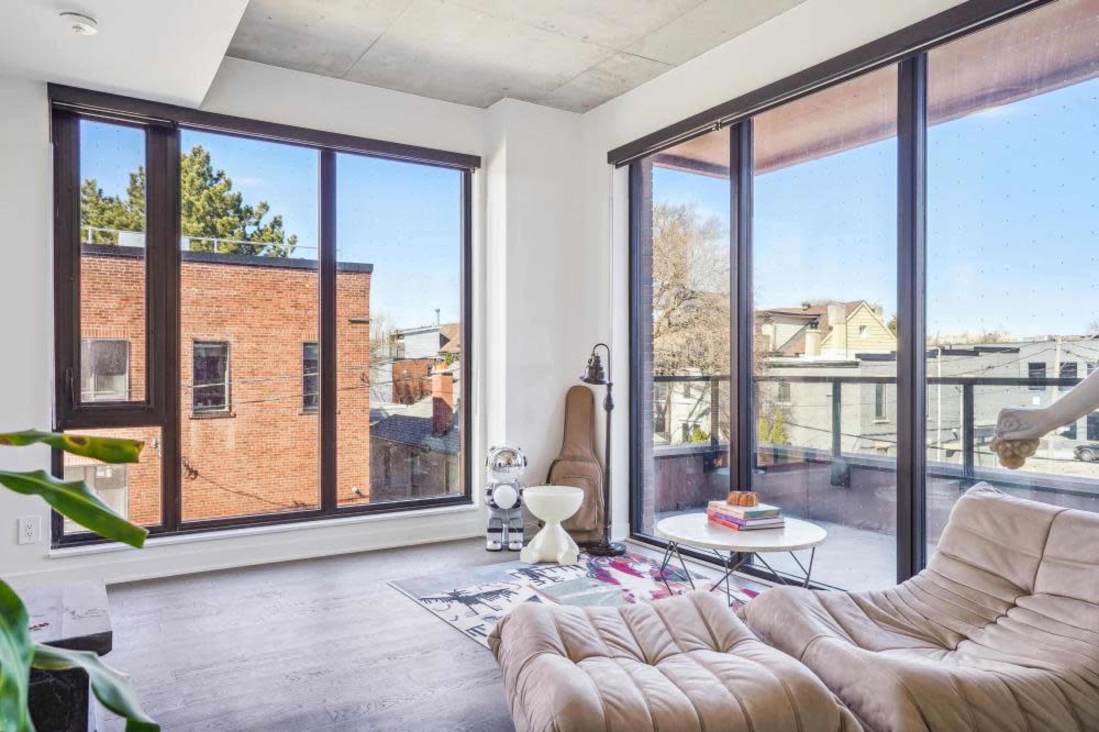 A modern living room with large windows allowing natural light to fill the space, featuring a cozy chair and a small table.