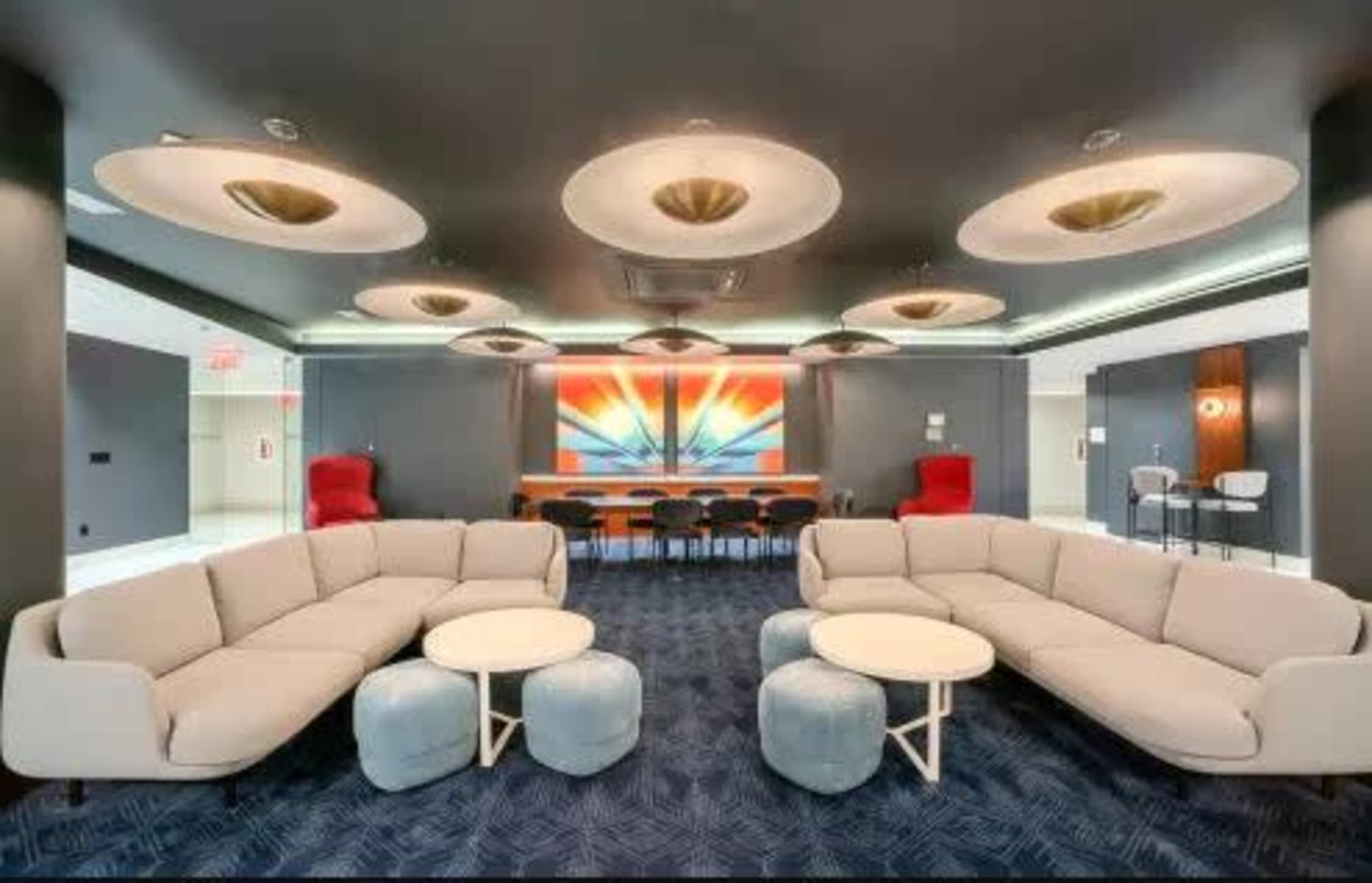 The image shows a modern lounge area with circular light fixtures, a large wall artwork, two stylish sofas, small round tables, and additional seating in the background.