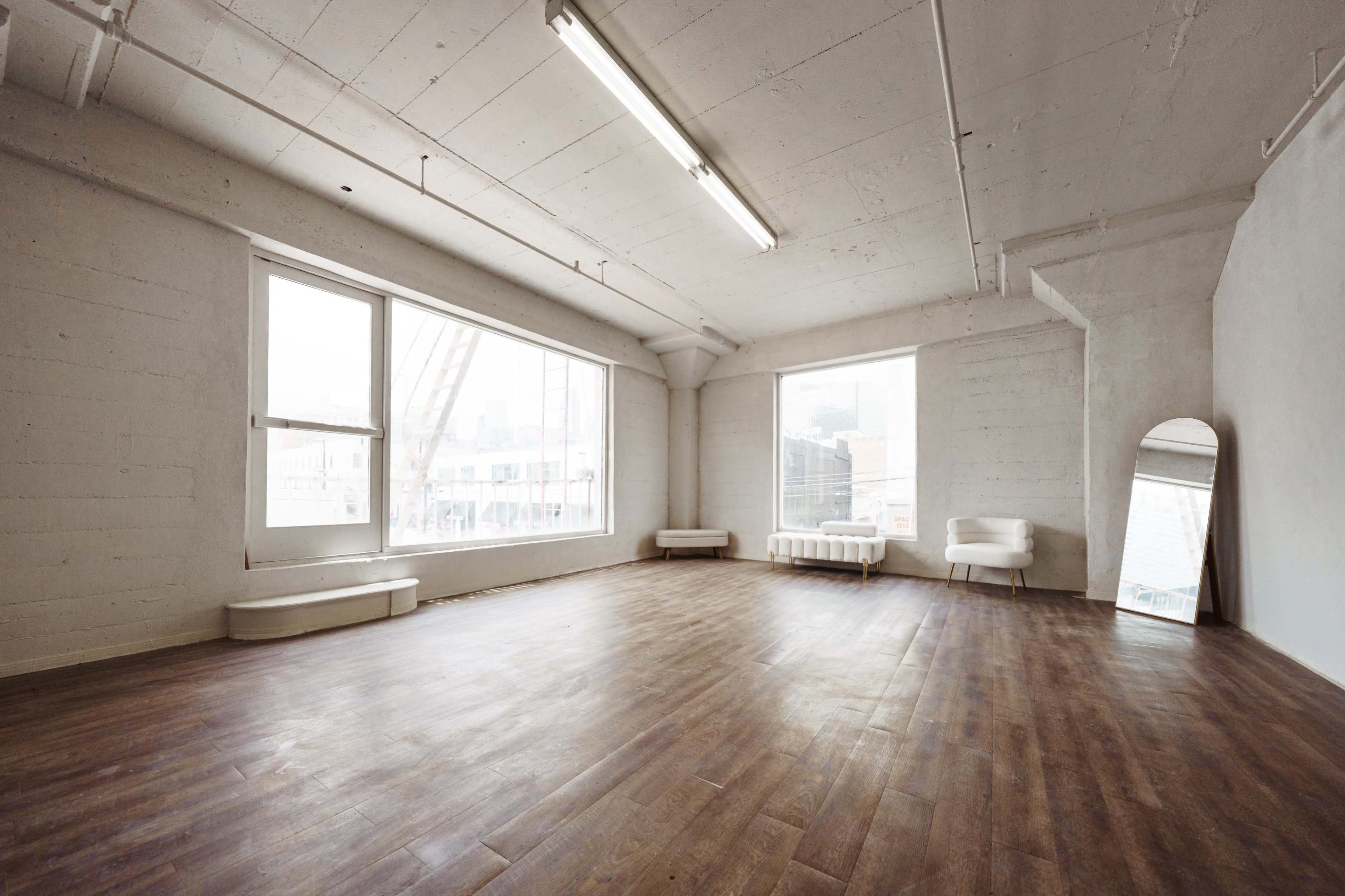 A spacious, minimally furnished room with large windows and wooden flooring.