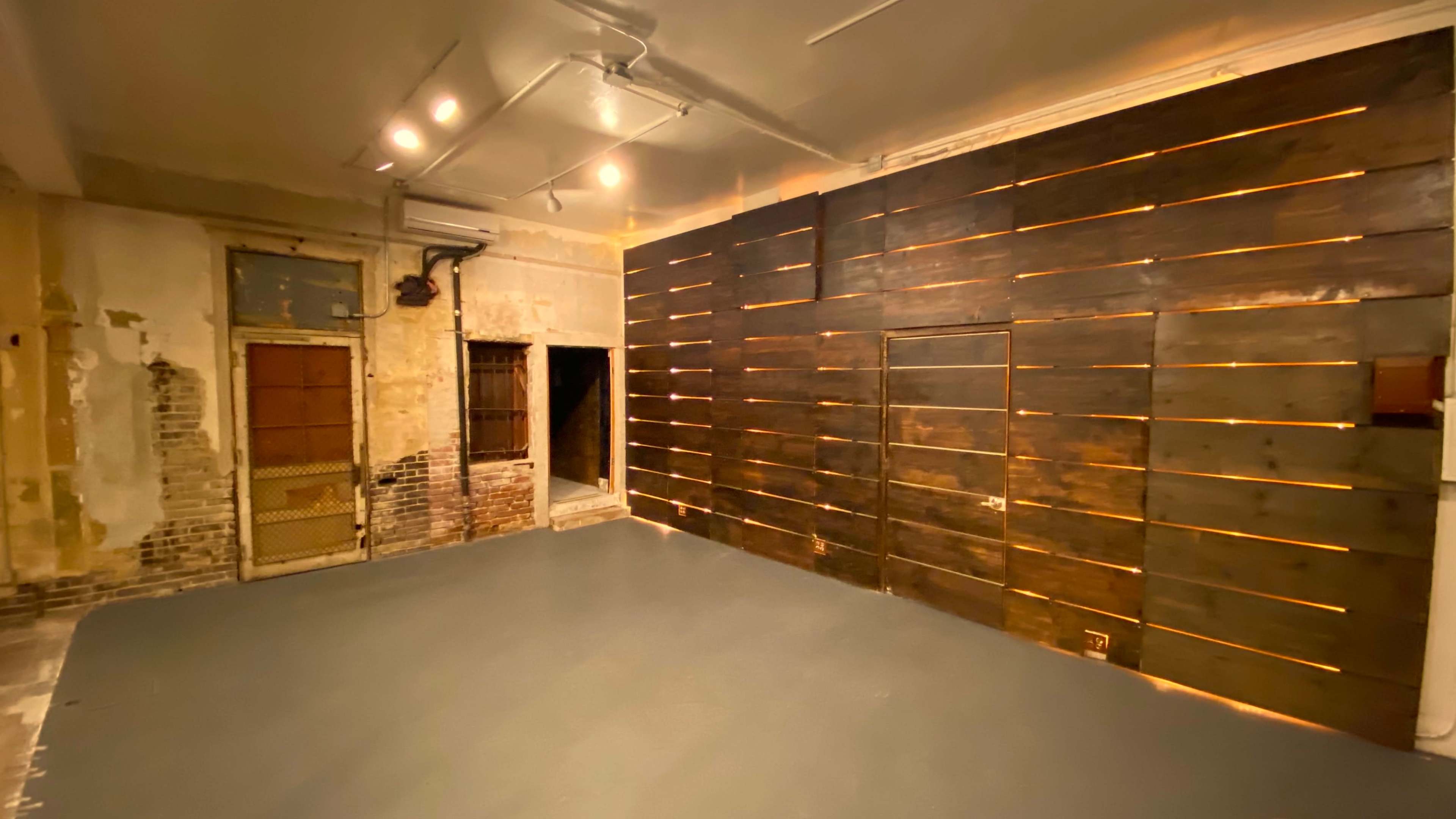An industrial-style room with a dark wooden wall featuring horizontal slats, bare brick on one side, and gray-painted flooring.
