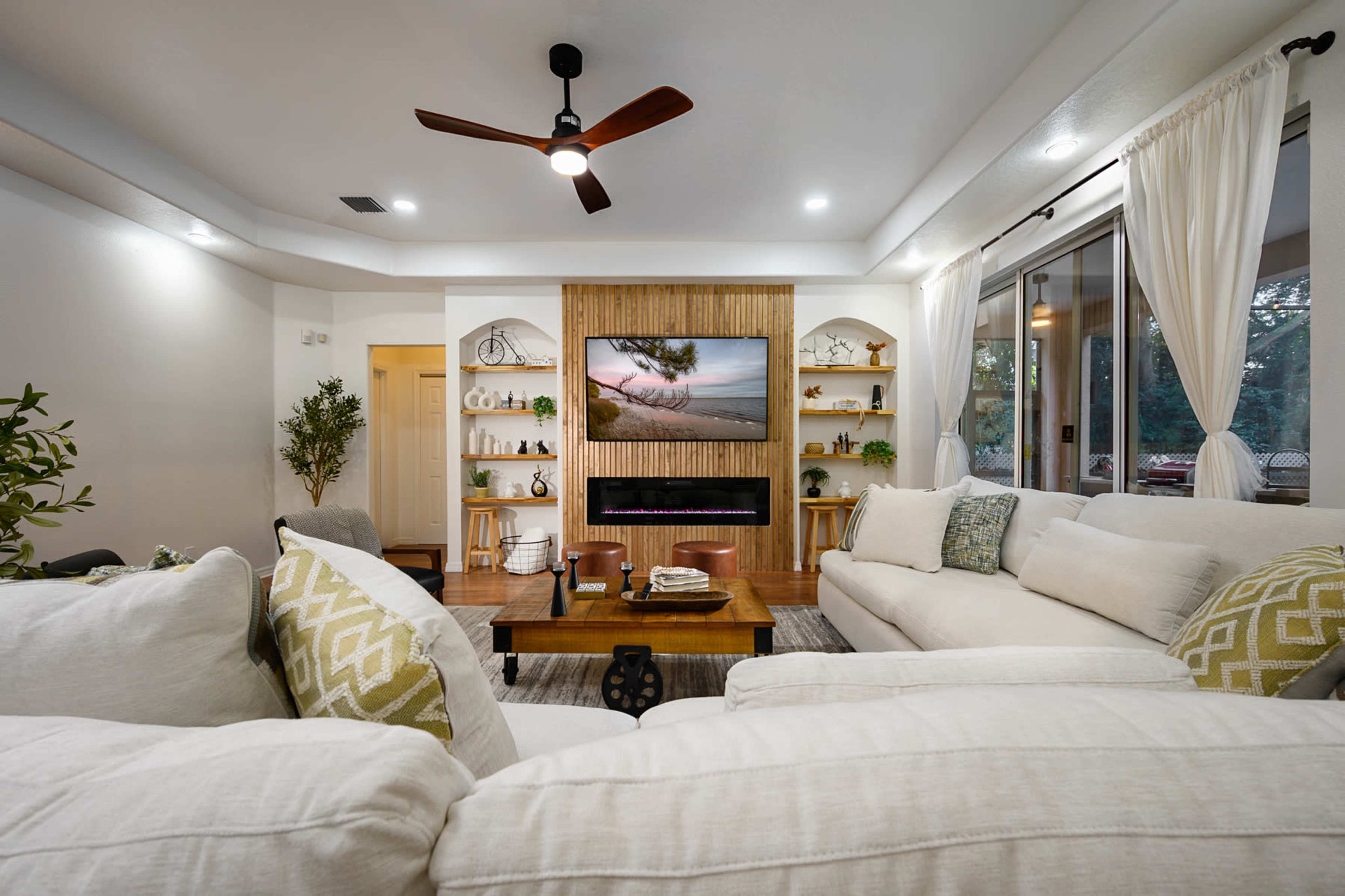 The living room features a large white sectional sofa, a wooden coffee table, and a wall-mounted television set within a wood-paneled display.