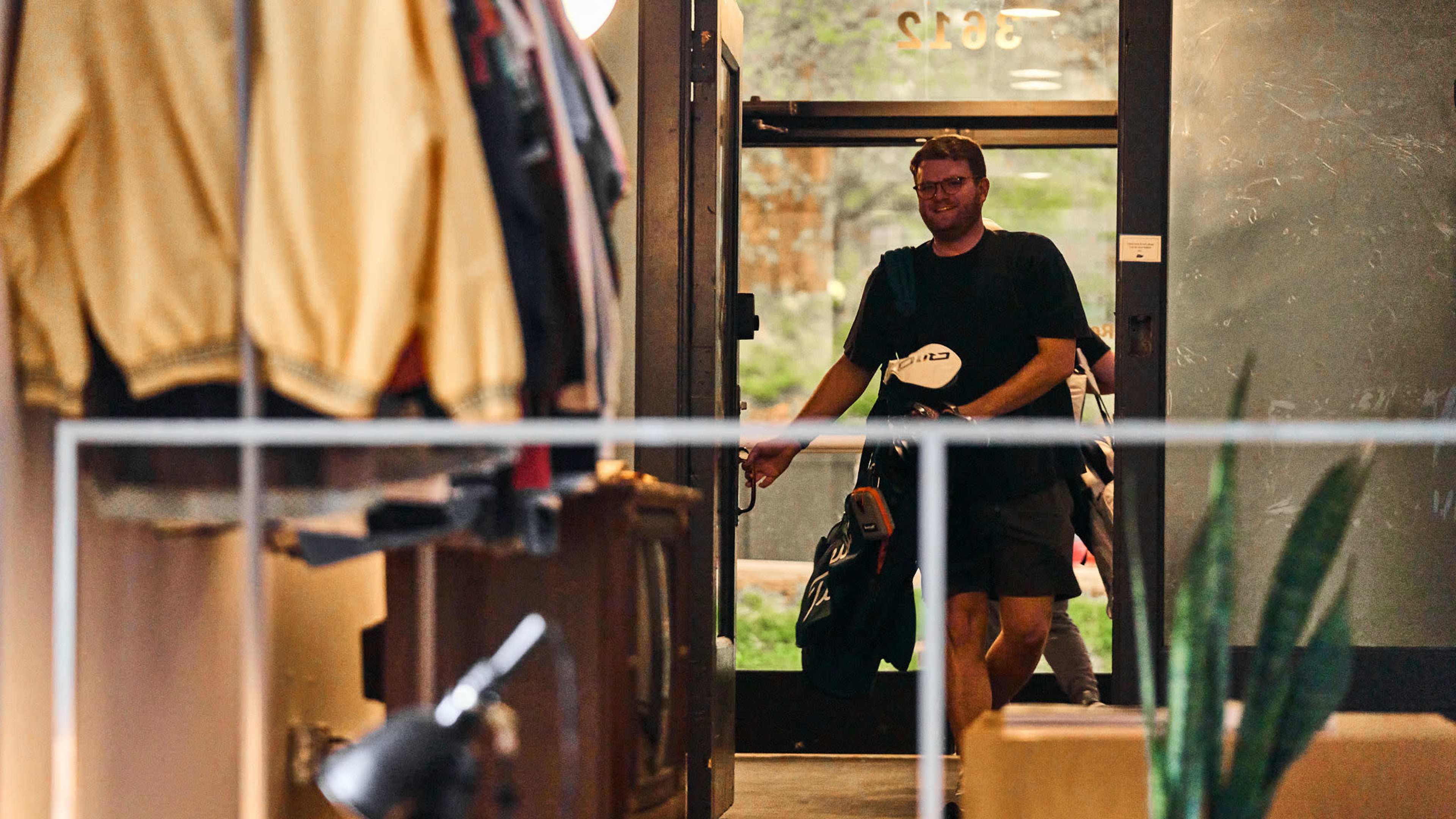 A man enters a clothing store through the front door while carrying a bag.