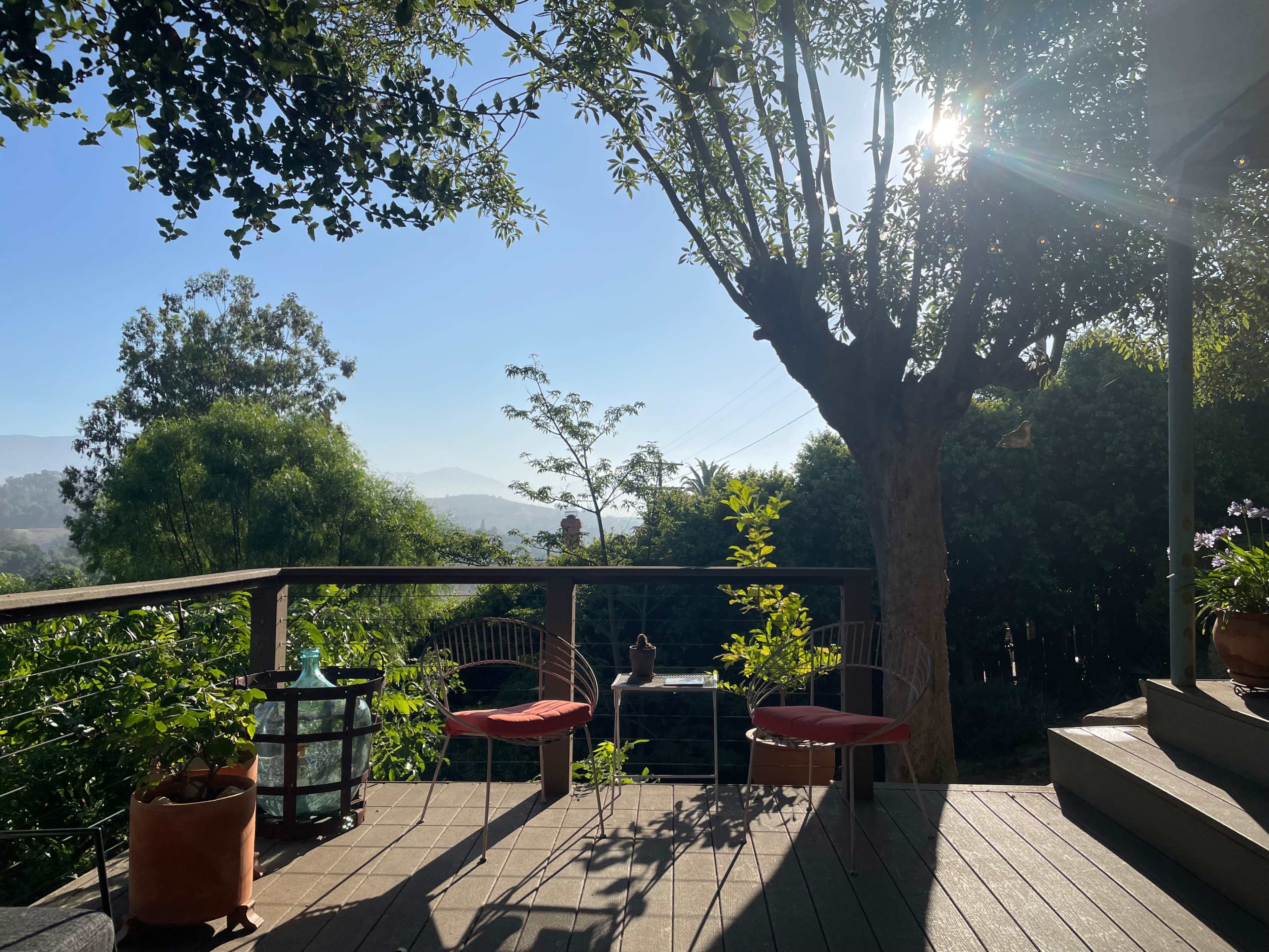 A wooden deck with two red chairs overlooks a green garden and distant hills under a clear blue sky.