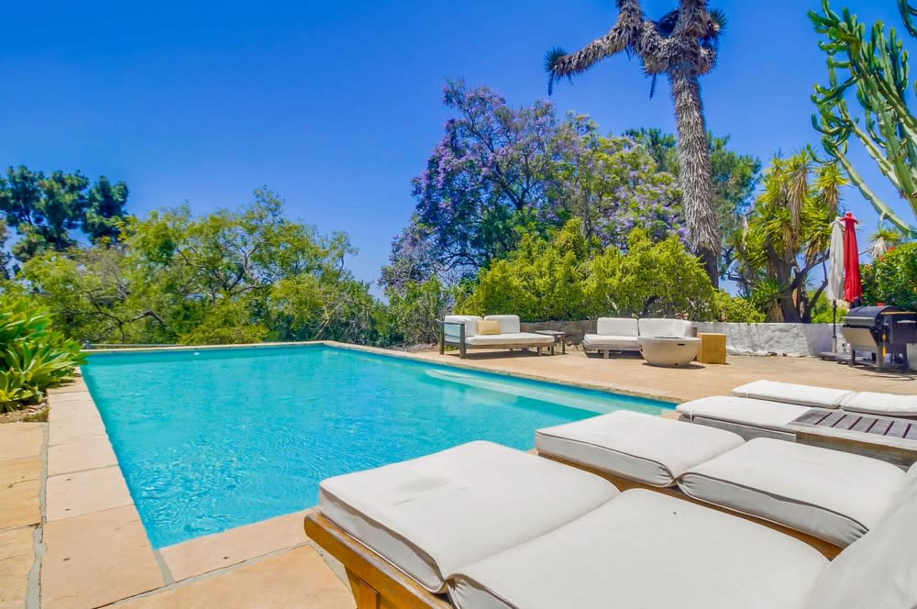 A crystal-clear swimming pool is surrounded by lush greenery and a sunny patio area with lounge chairs.