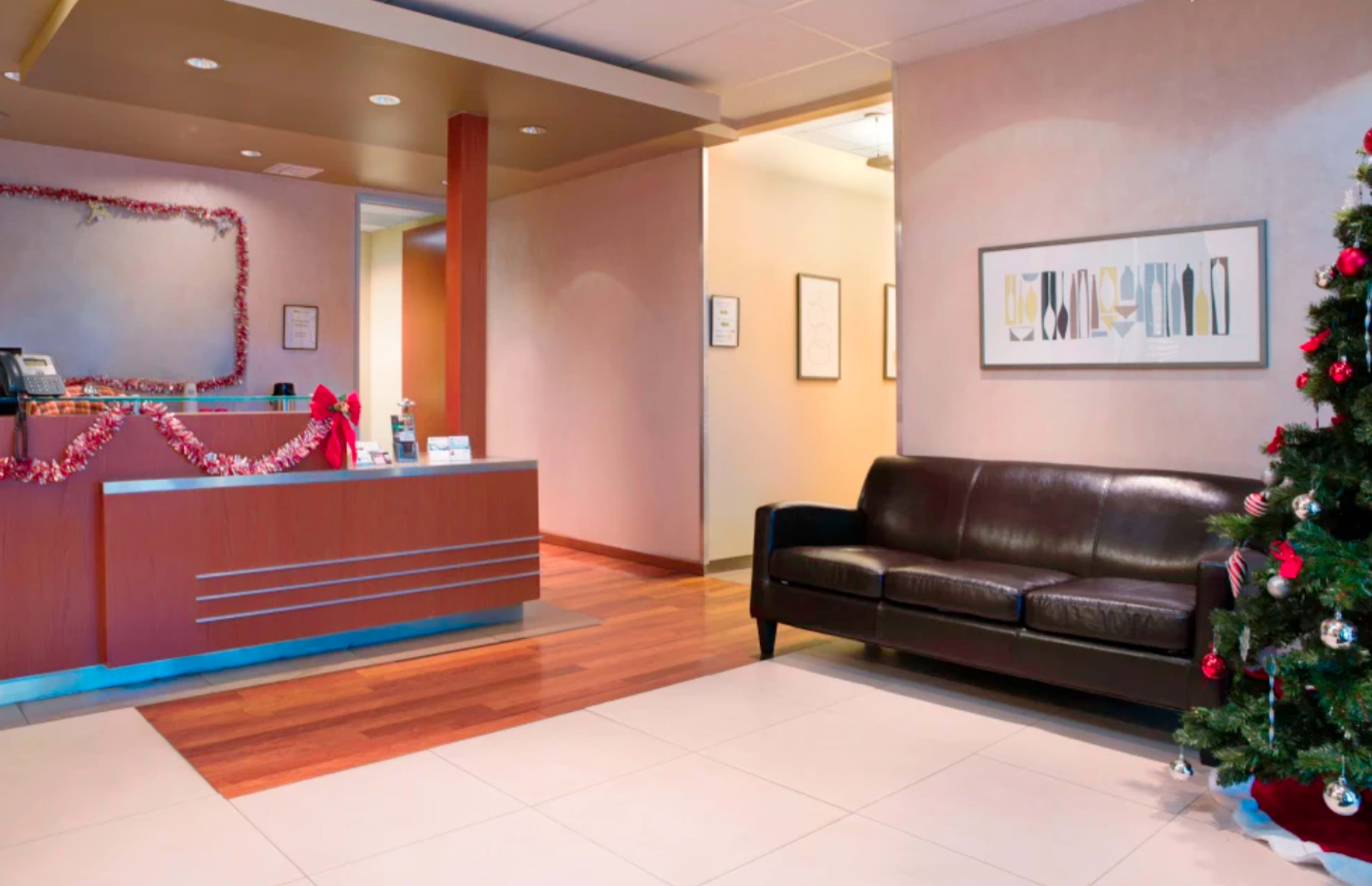 A reception area with a front desk decorated for the holidays, a dark sofa, and a Christmas tree in the corner.