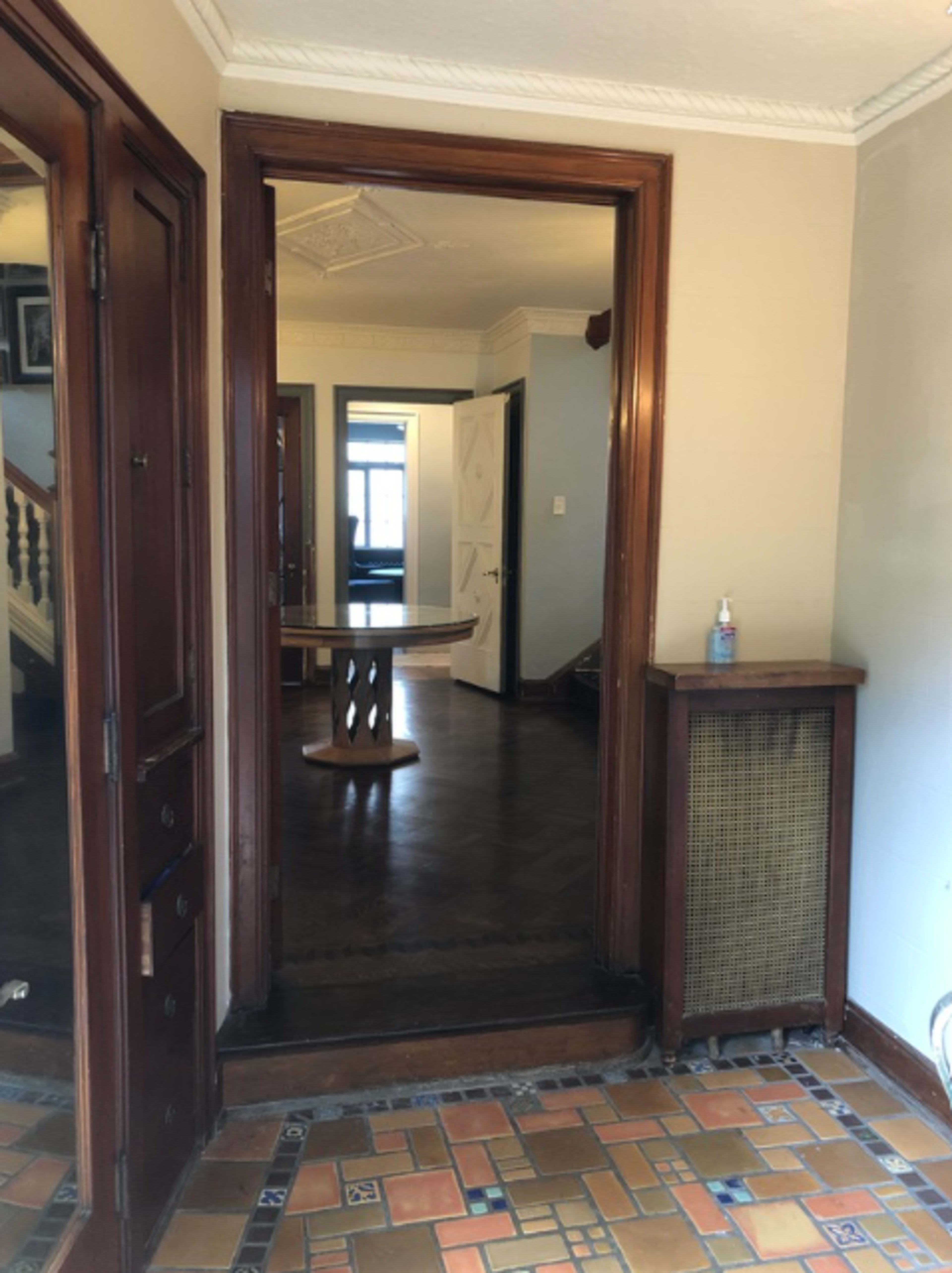 A hallway with wooden trim, featuring a mirror on the left side and a view into a room with a round table ahead.