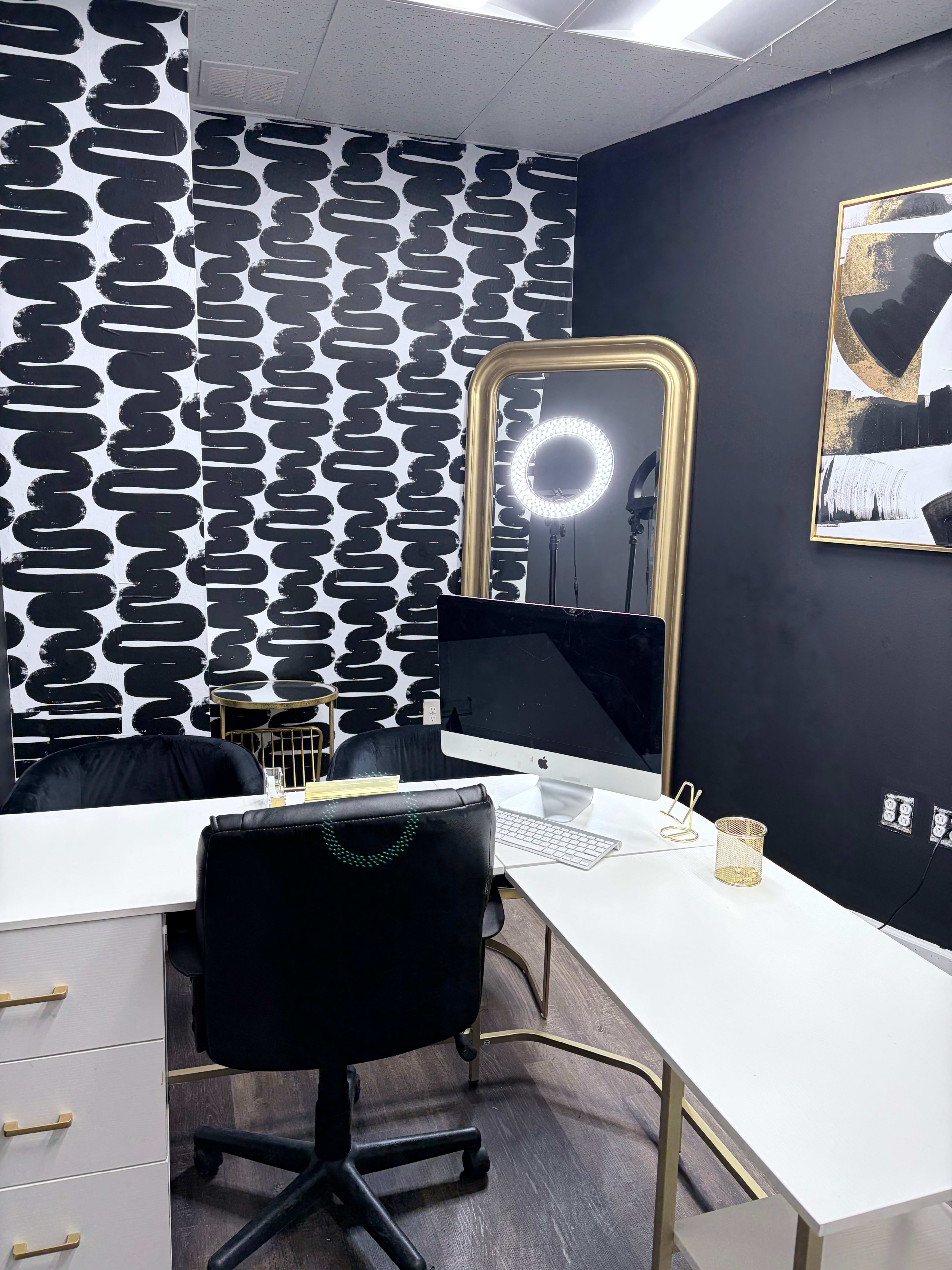 The image shows a modern office space with a large mirror, a computer desk, and a ring light, all set against a black and white patterned wall.