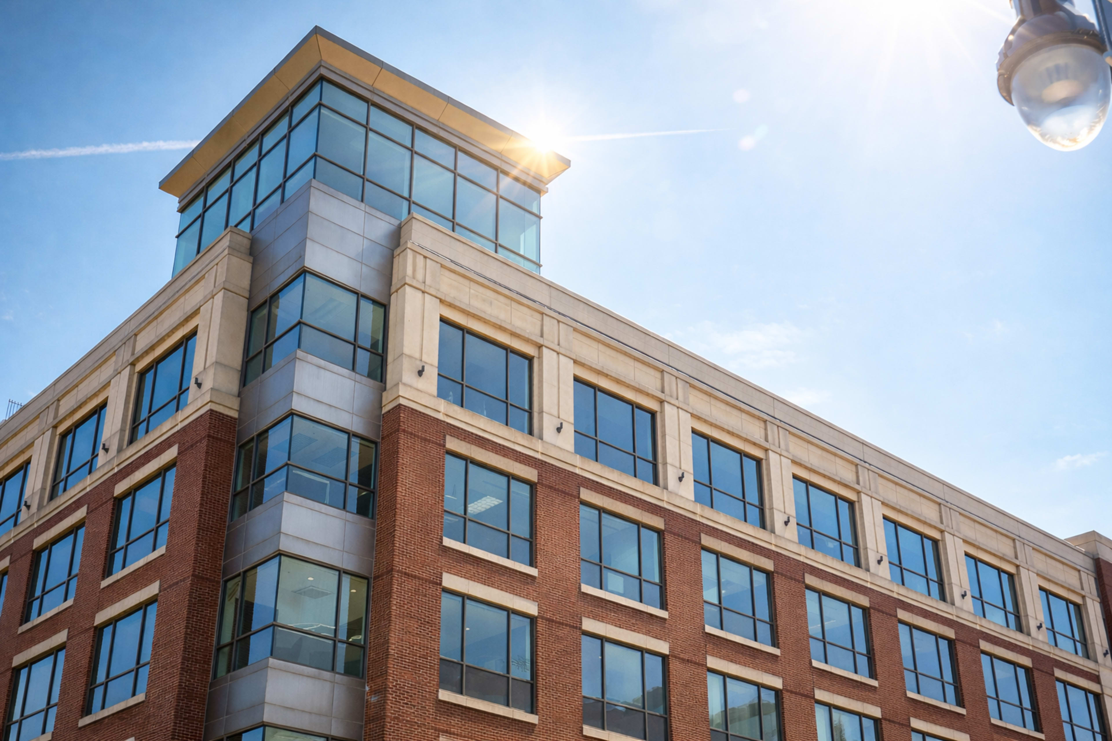 The image shows a modern brick and glass building with large windows under a clear blue sky.