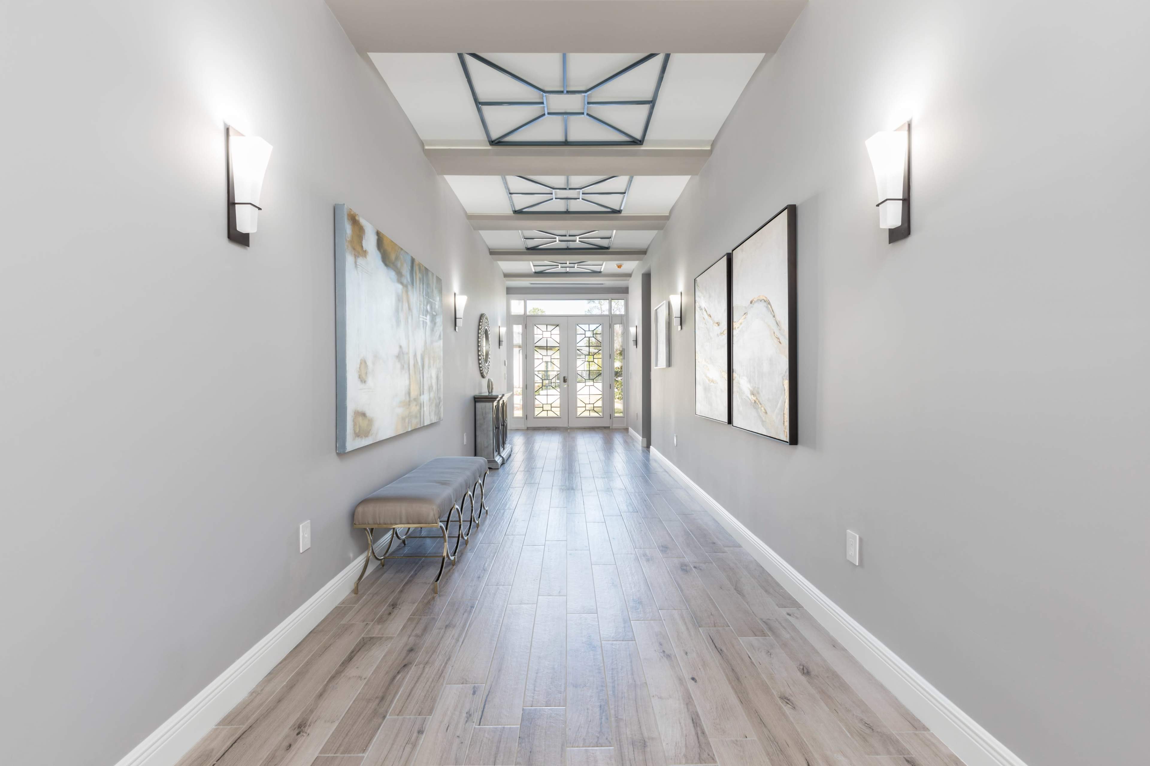 A well-lit hallway features a bench, wall art, and a door leading to the outside.