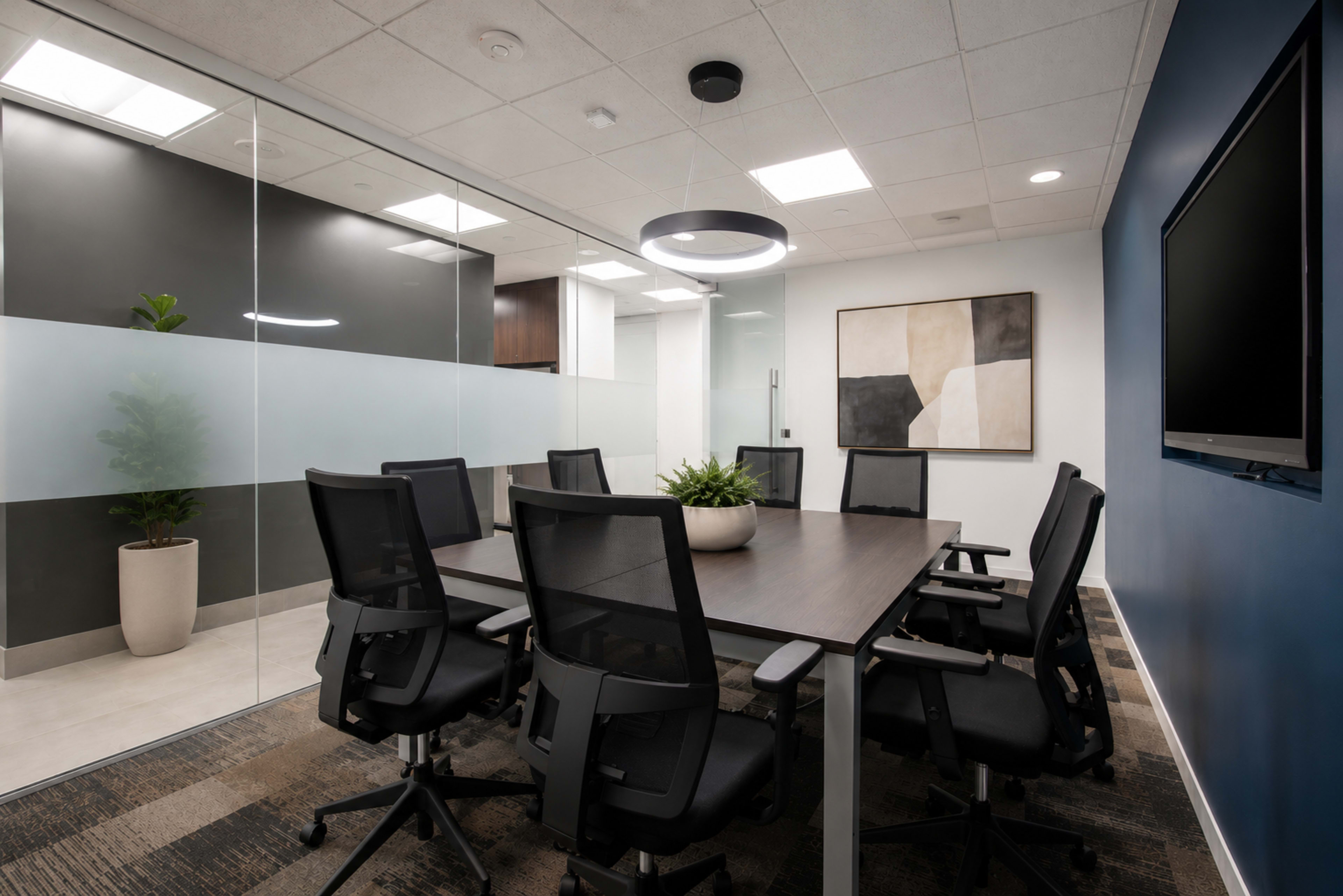 A modern conference room features a large table surrounded by ergonomic chairs, with glass walls and a plant in a pot.