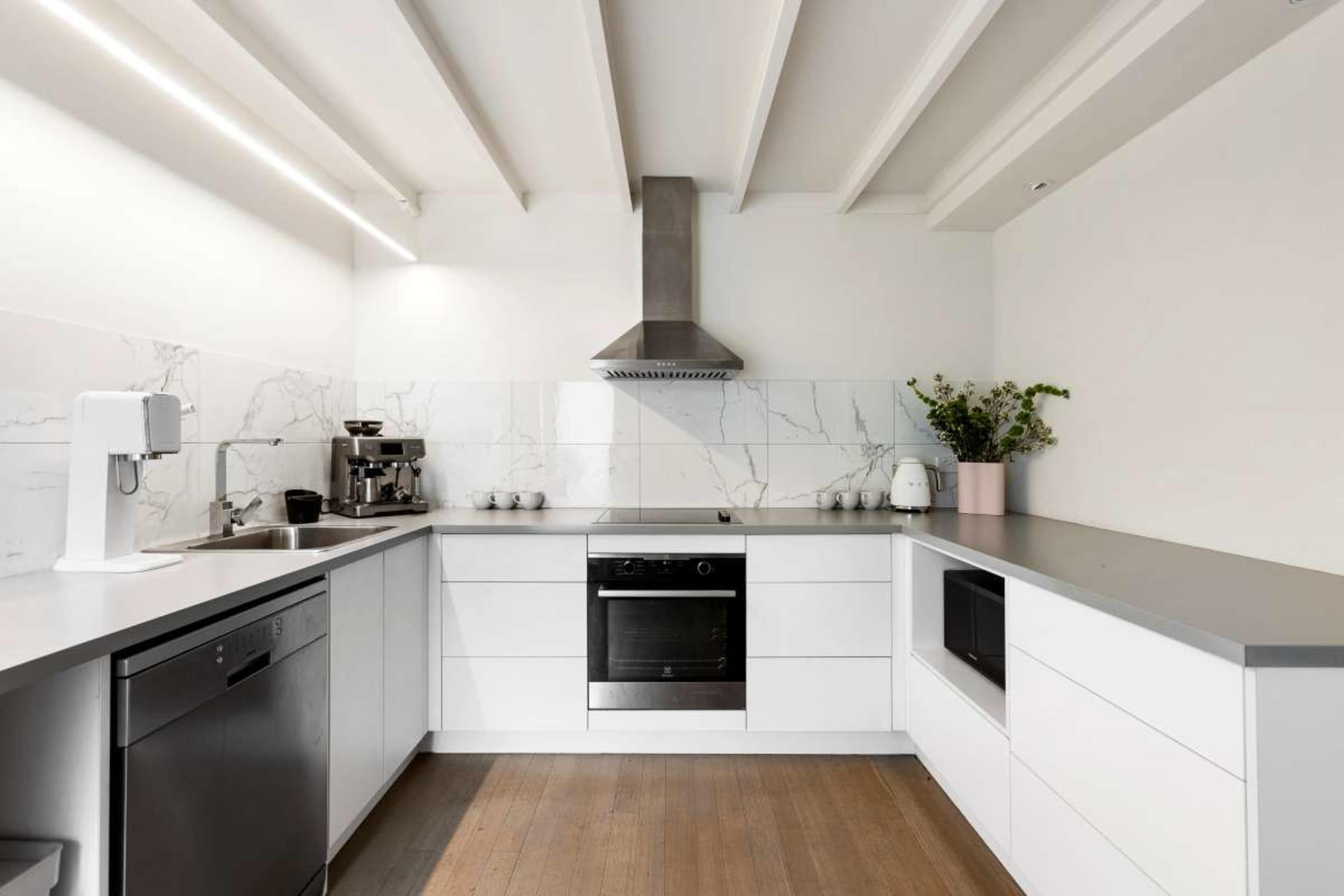 The image shows a modern kitchen featuring white cabinetry, a stainless steel range hood, and a marble backsplash.