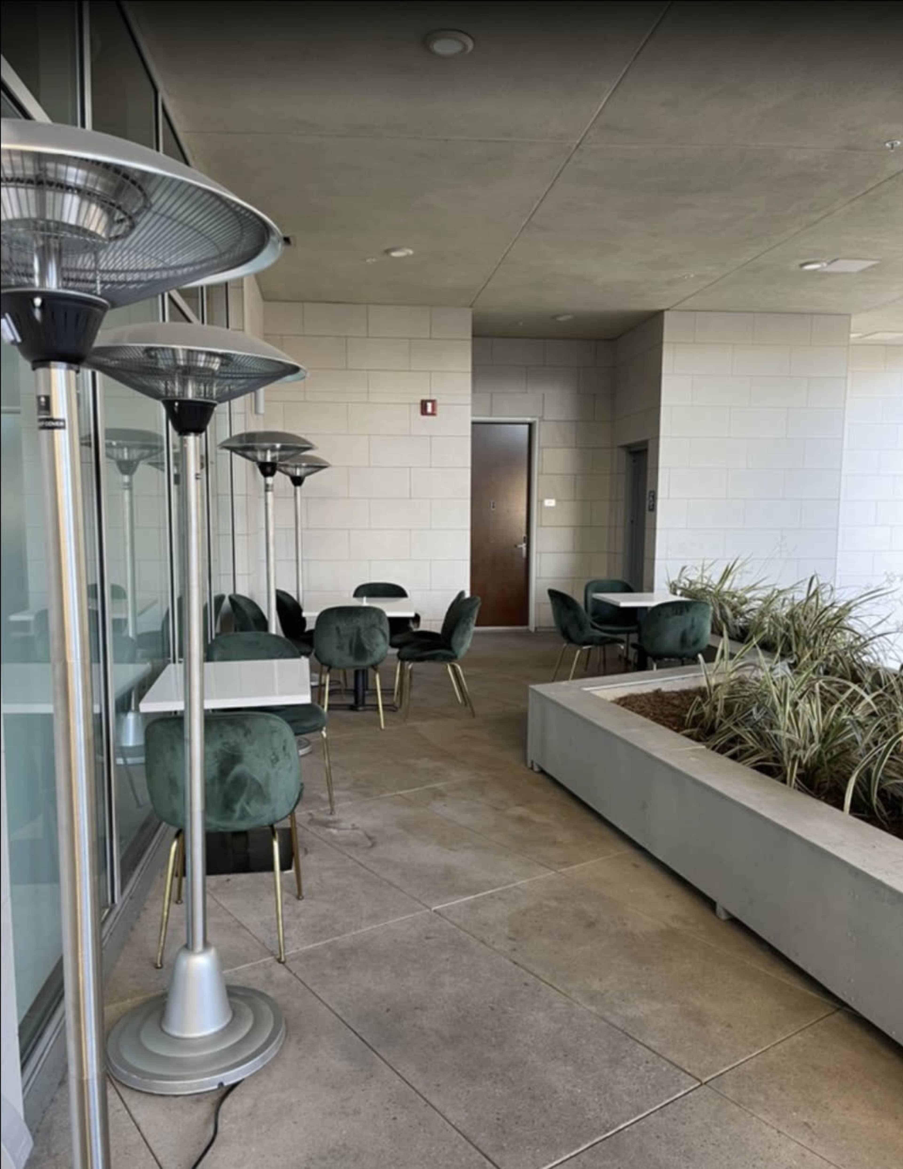 A covered outdoor seating area features several tables and chairs alongside a planter and patio heaters.