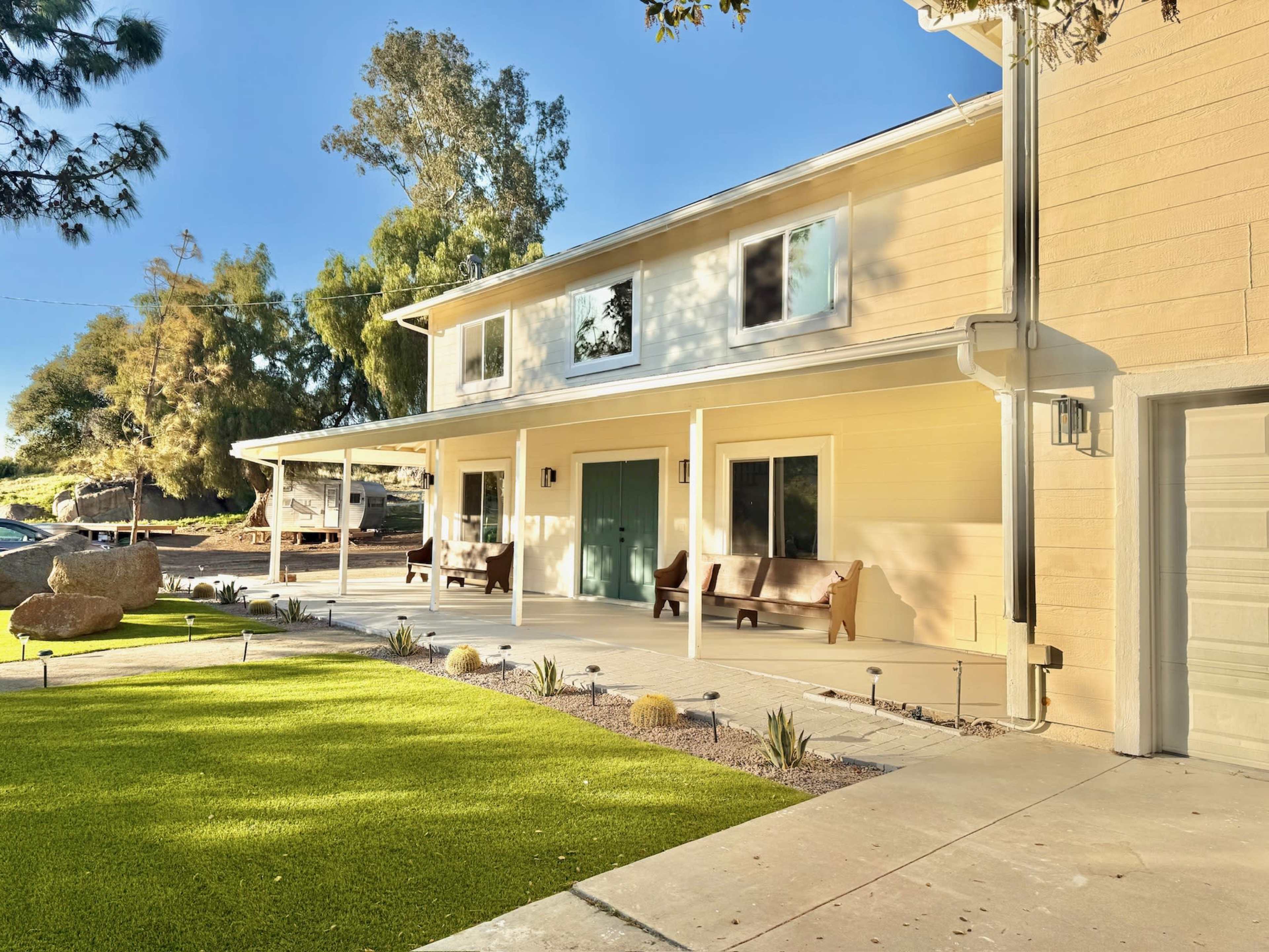 The image features a two-story house with a covered porch, situated in a landscaped area with green grass and rock accents.