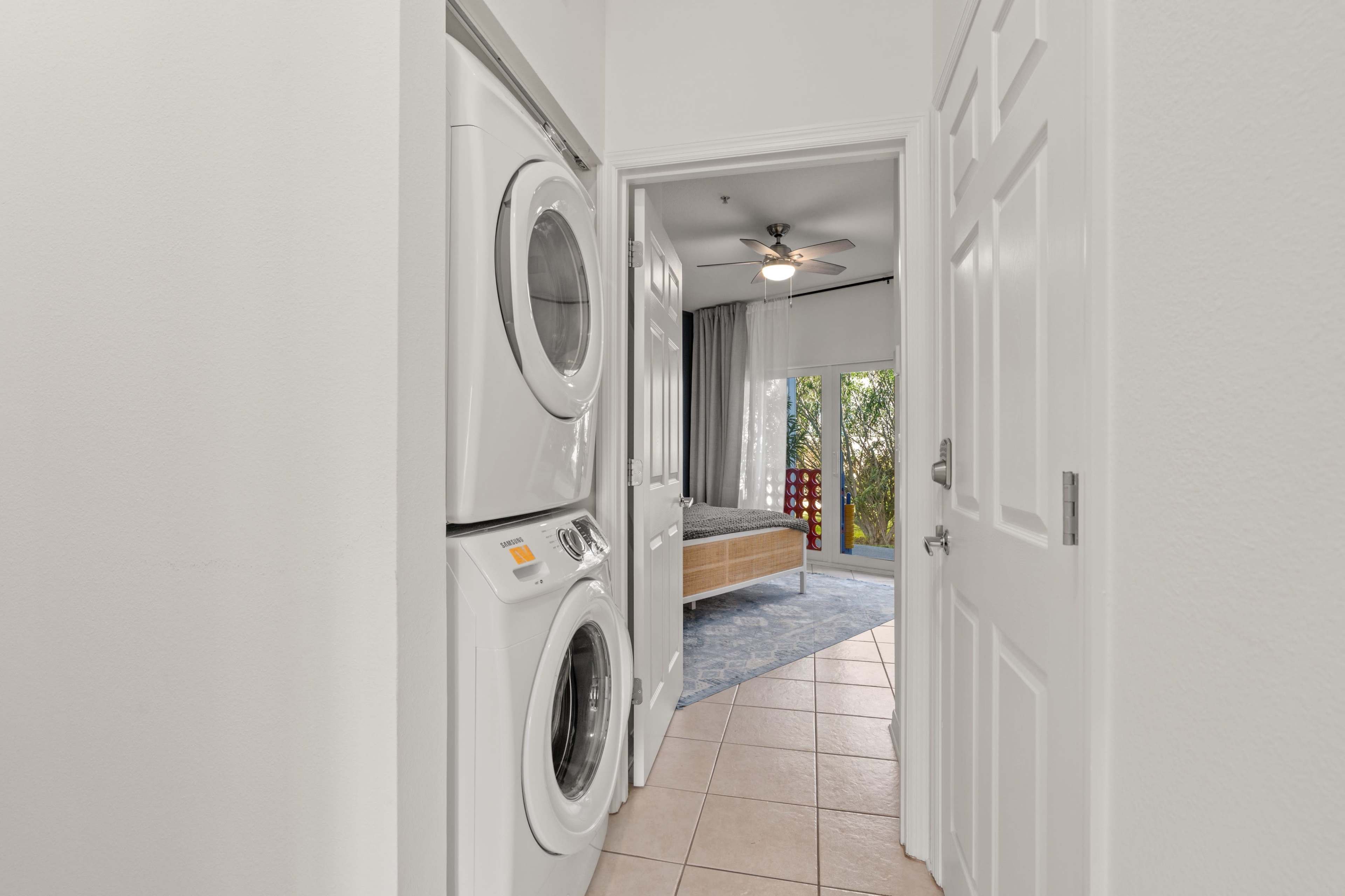 A laundry area with stacked washers and dryers, leading to a bedroom through an open door.