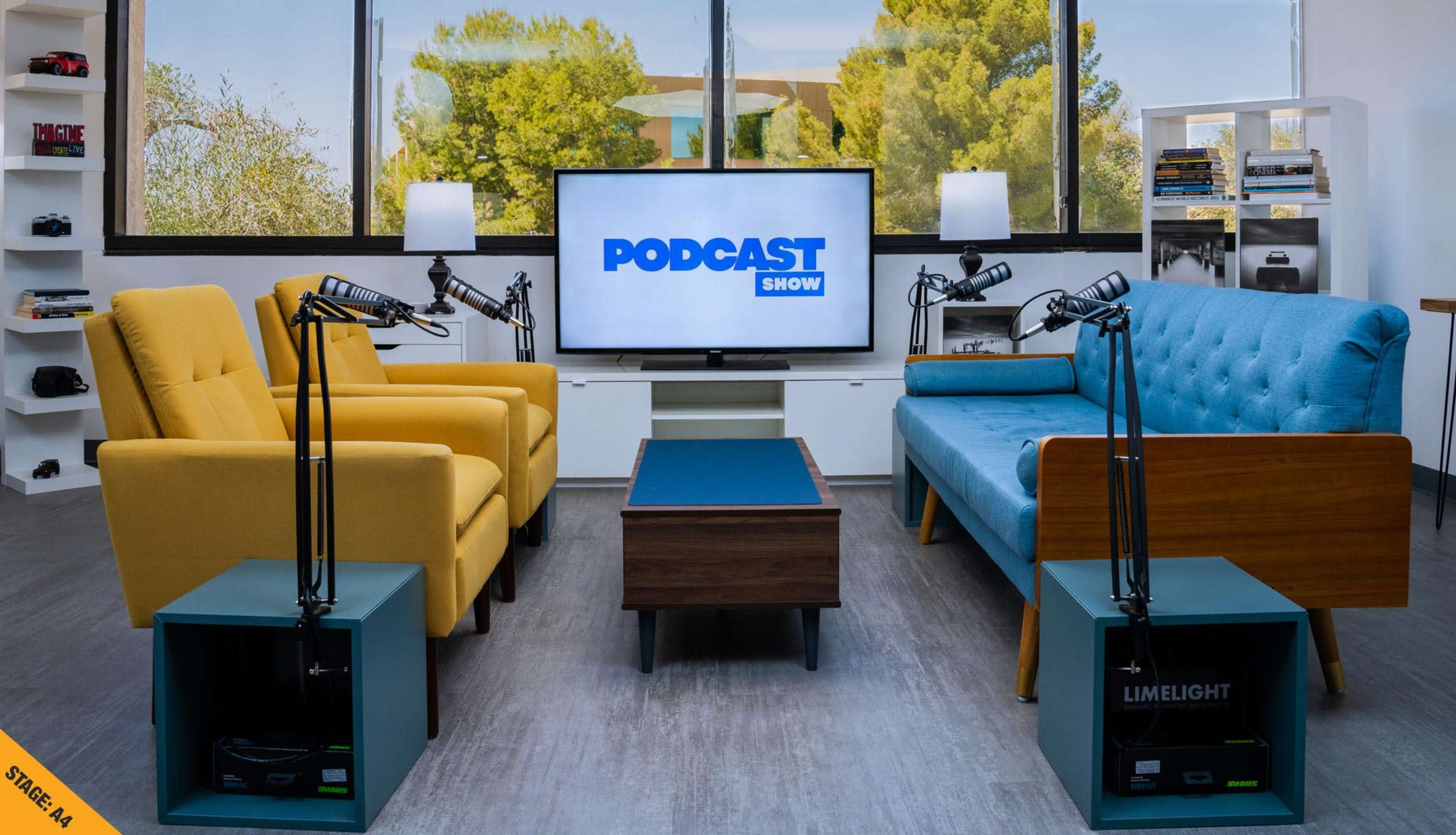 The image shows a modern podcast studio setup with two chairs, a coffee table, and a large screen displaying the words "PODCAST SHOW."