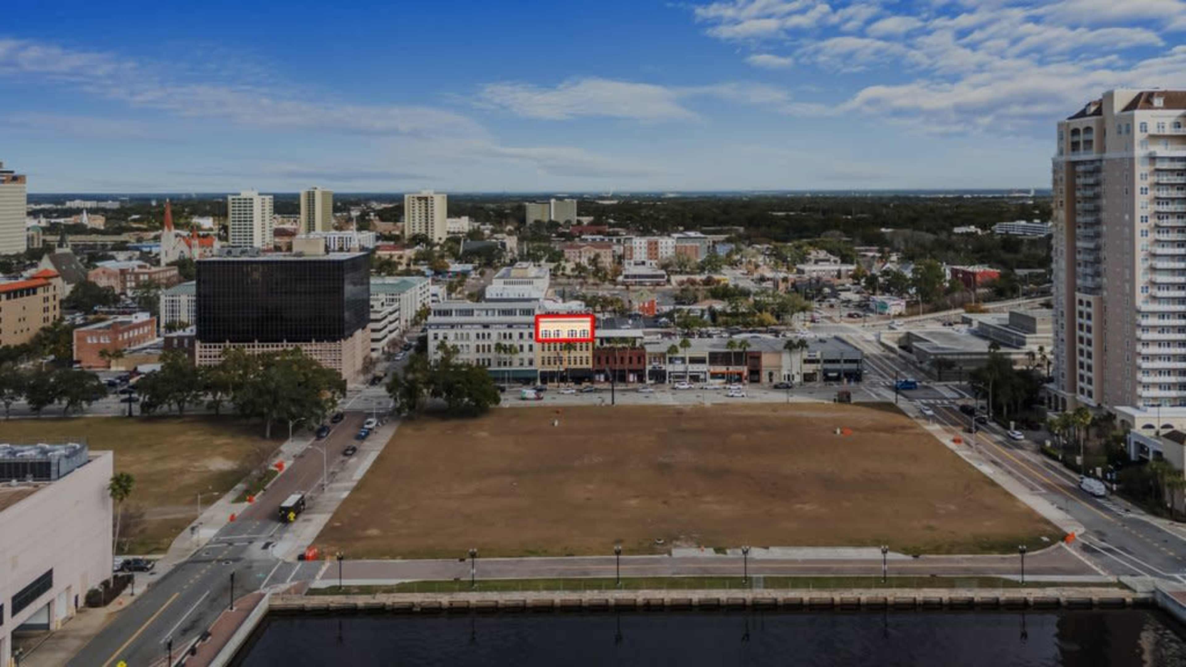 The image shows an aerial view of a cityscape featuring a clear sky, buildings, and an open area with grass.