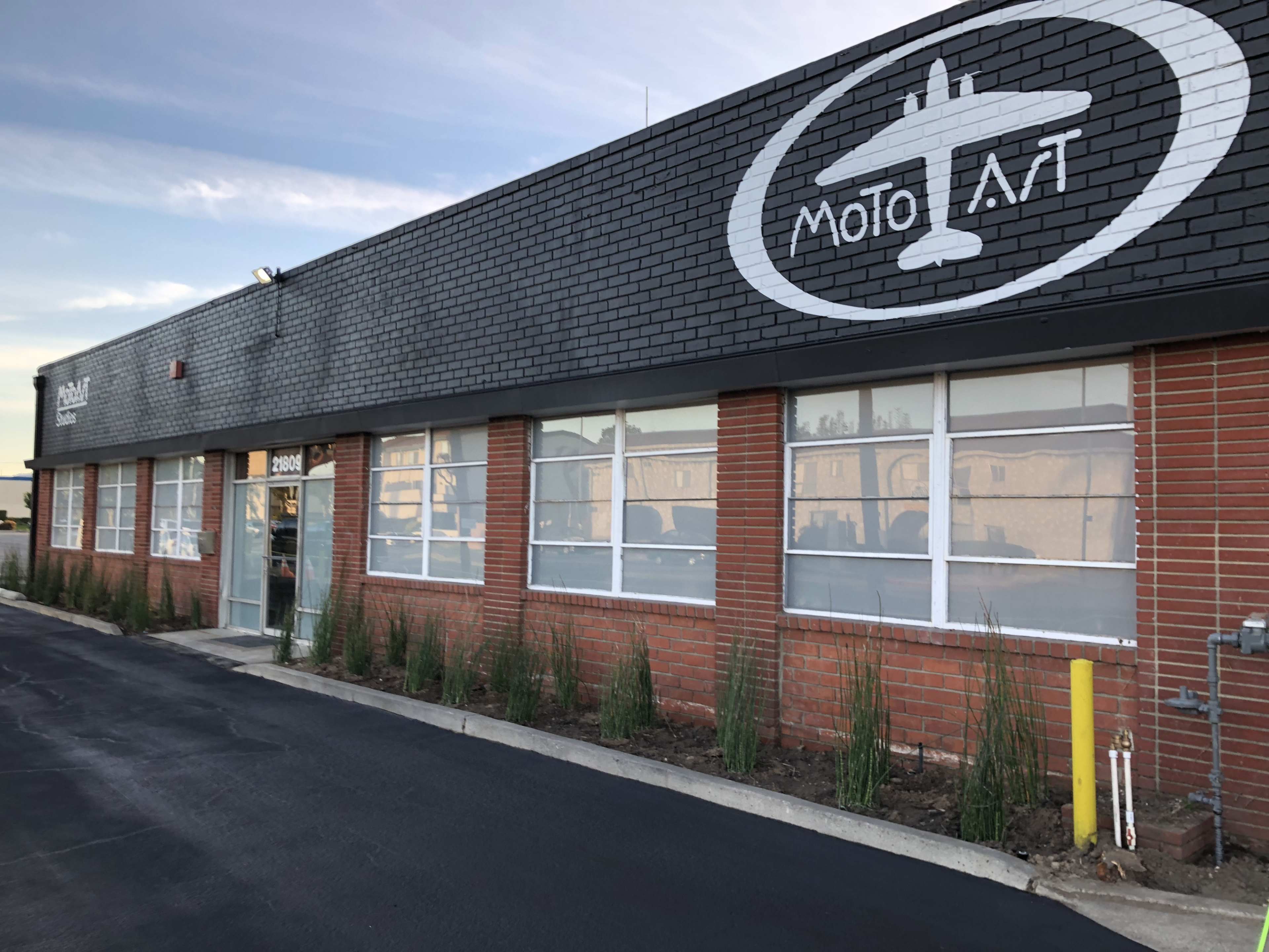 The image shows a brick building with large windows, featuring a logo of an aircraft and the text "Moto A.T." on its facade.