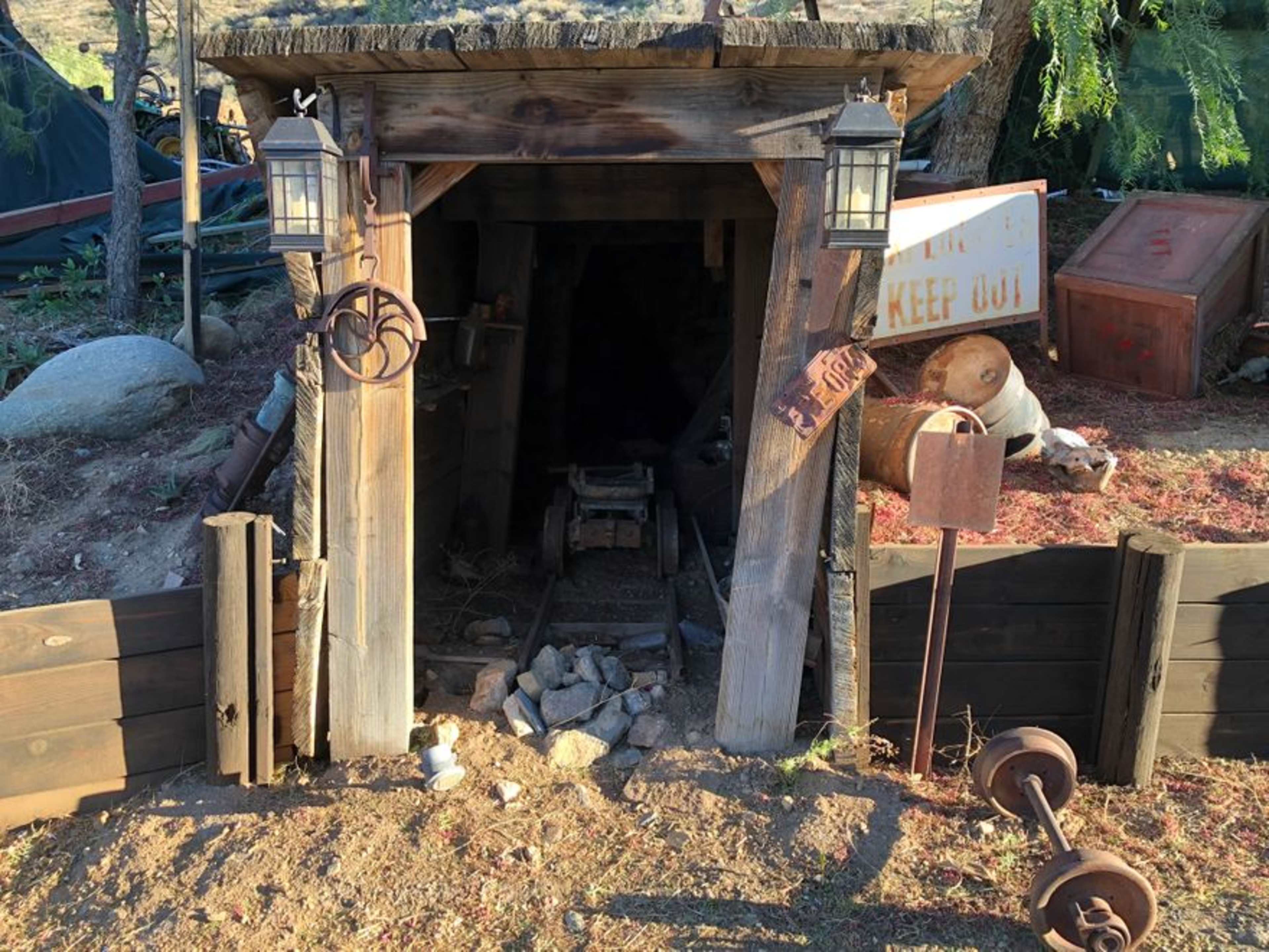 A rustic wooden mine entrance with a small cart, surrounded by rocks and old mining equipment.