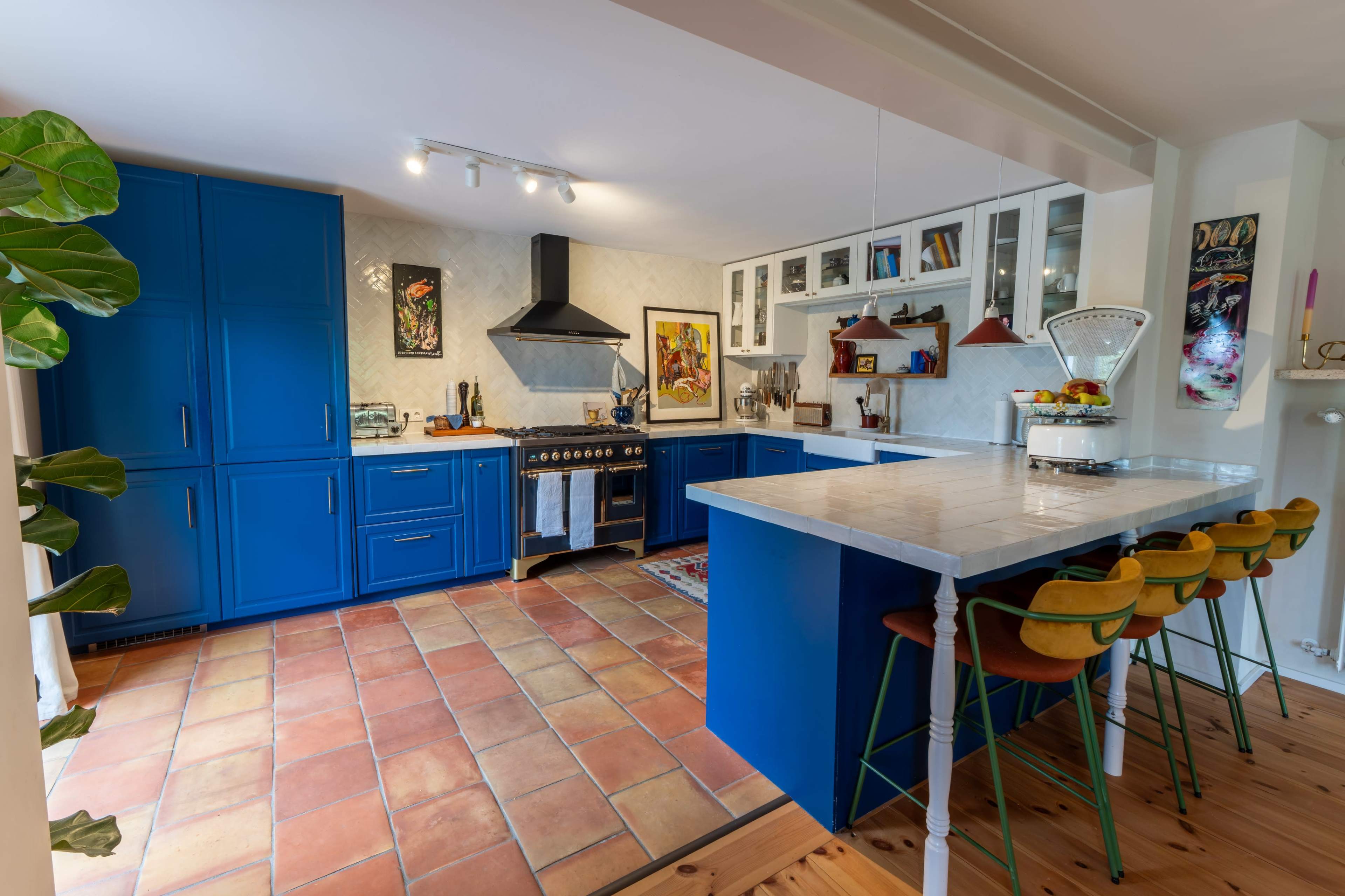 The kitchen features blue cabinets, a black range hood, and an island with bar stools on a tiled floor.