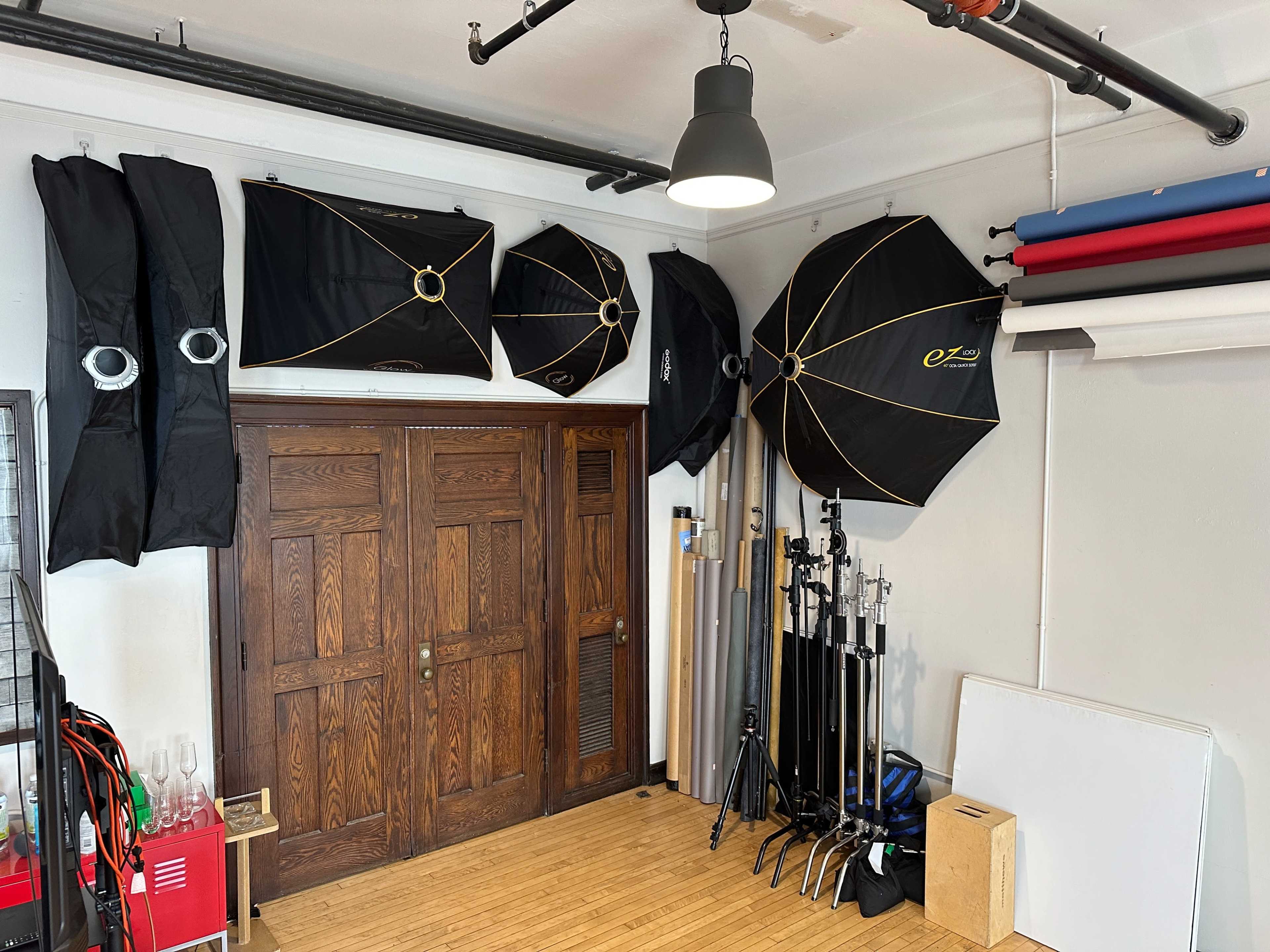 A room with several photography light umbrellas mounted on the walls, alongside various photography gear and props stored on the floor.