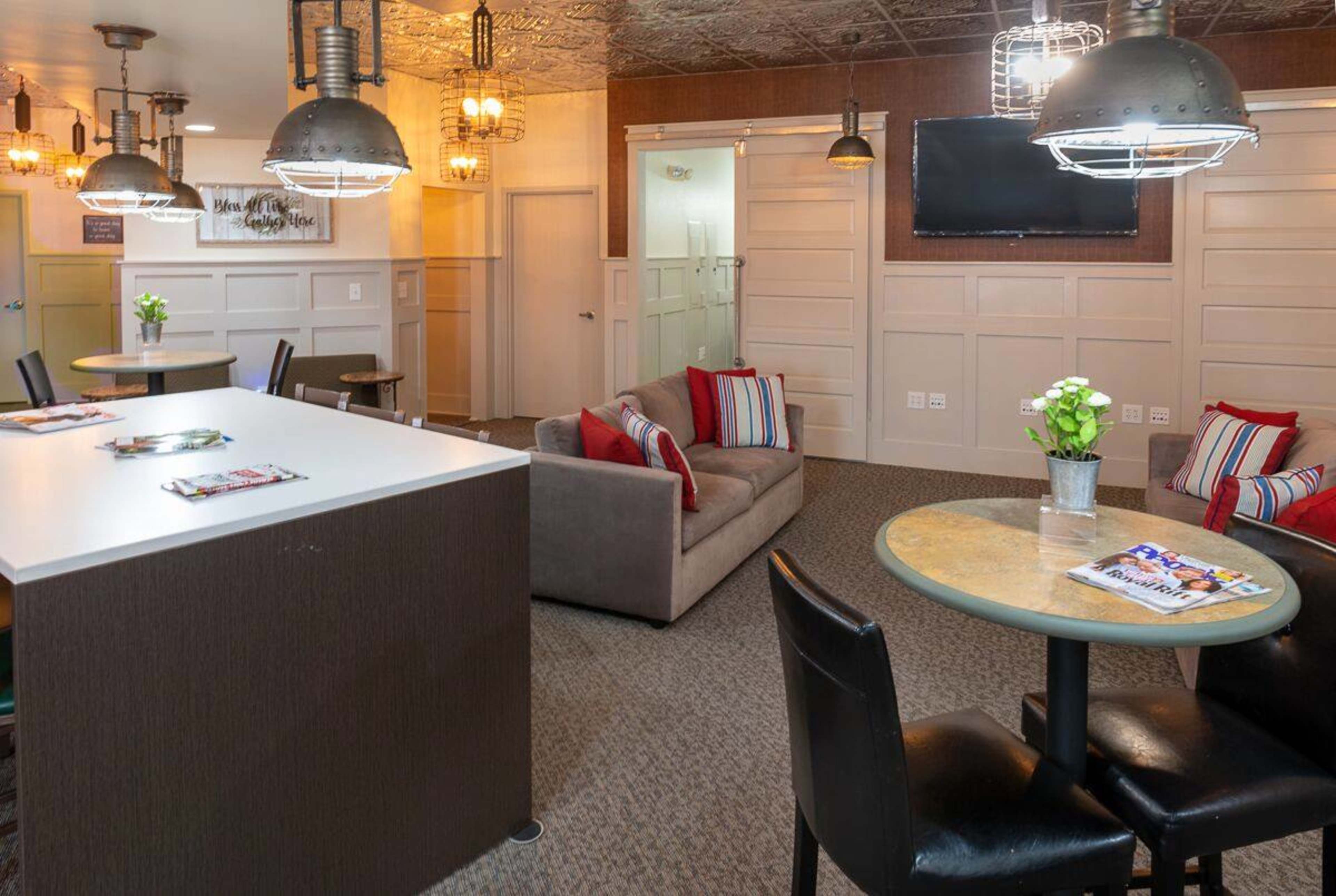 A cozy lounge area with a sofa, tables, and modern lighting fixtures, featuring a television on the wall and decorative items on the tables.
