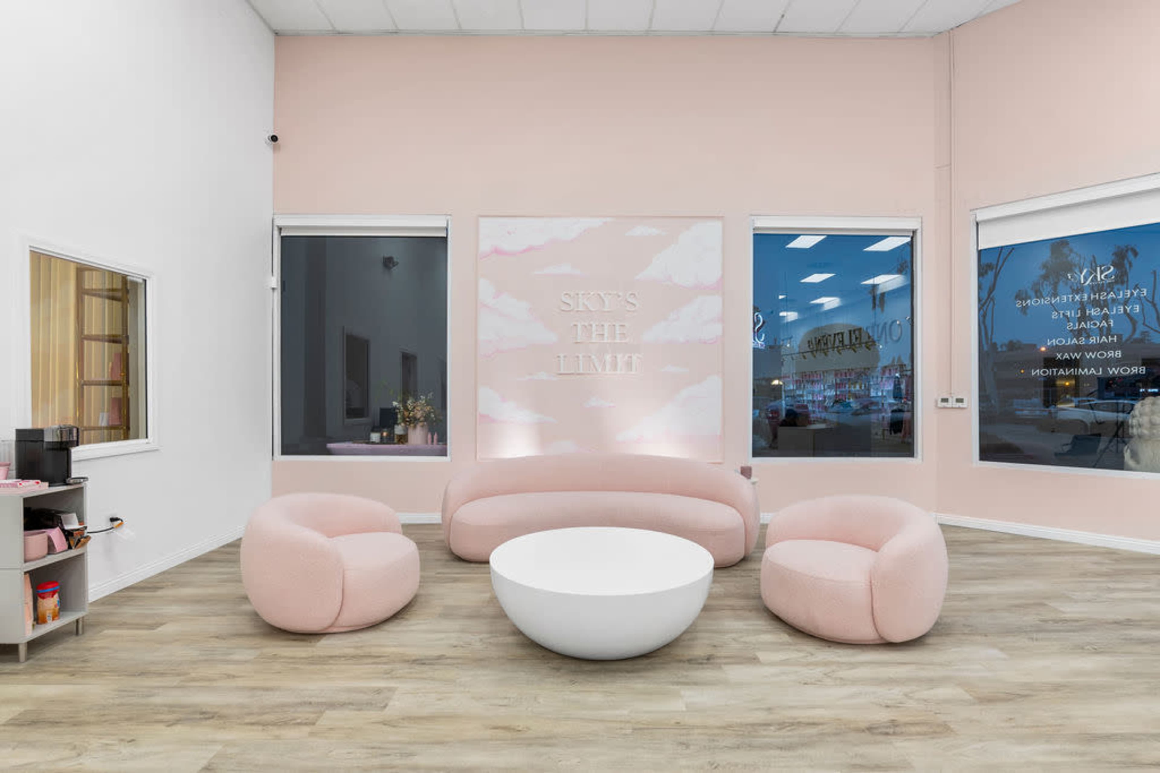 A modern interior with pink walls, a circular white table, and round pink seating in a brightly lit space.