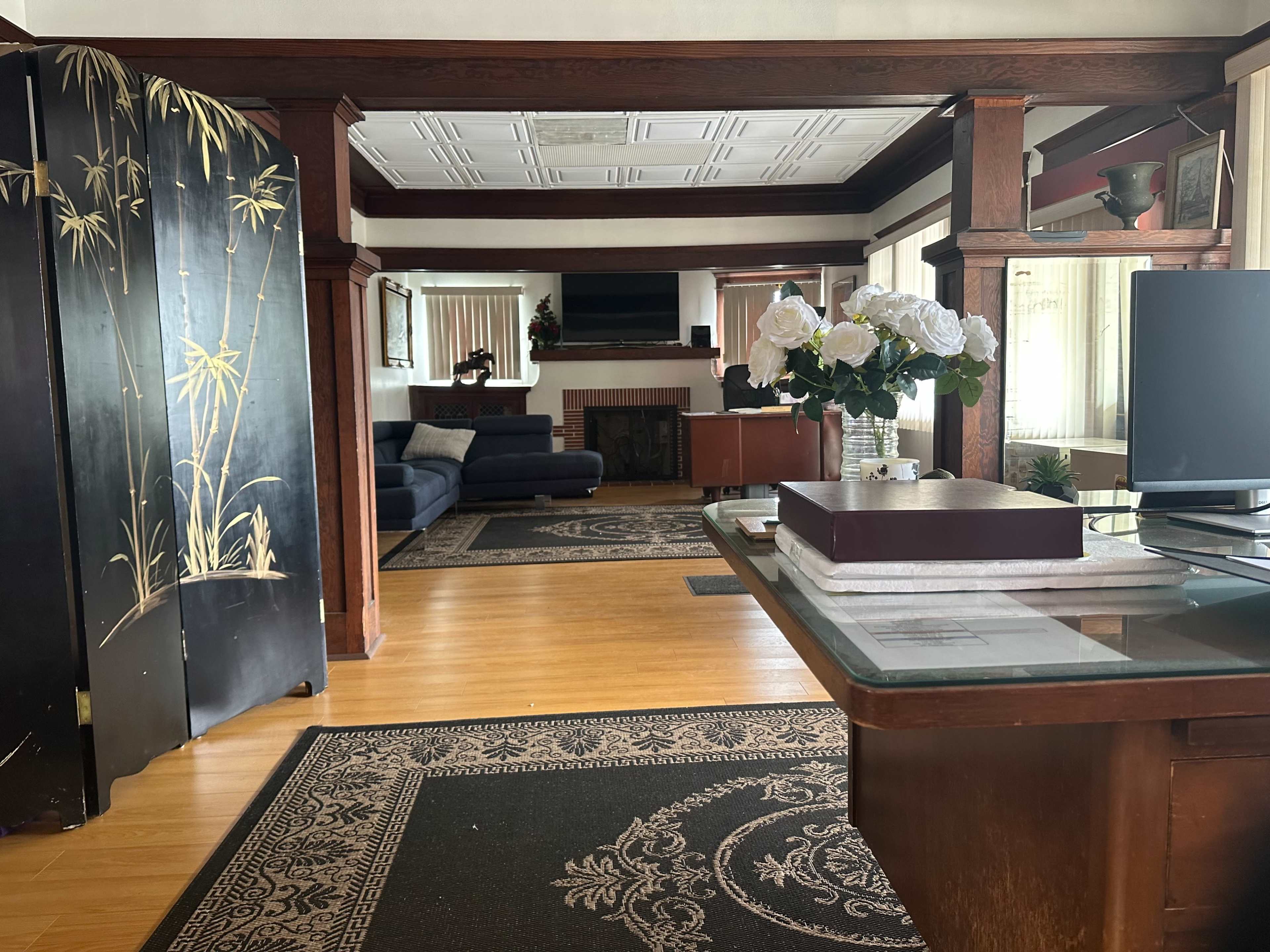 The image shows a spacious living area with wooden structural elements, a dark blue sofa, and a decorative screen, leading to a fireplace and television in the background.