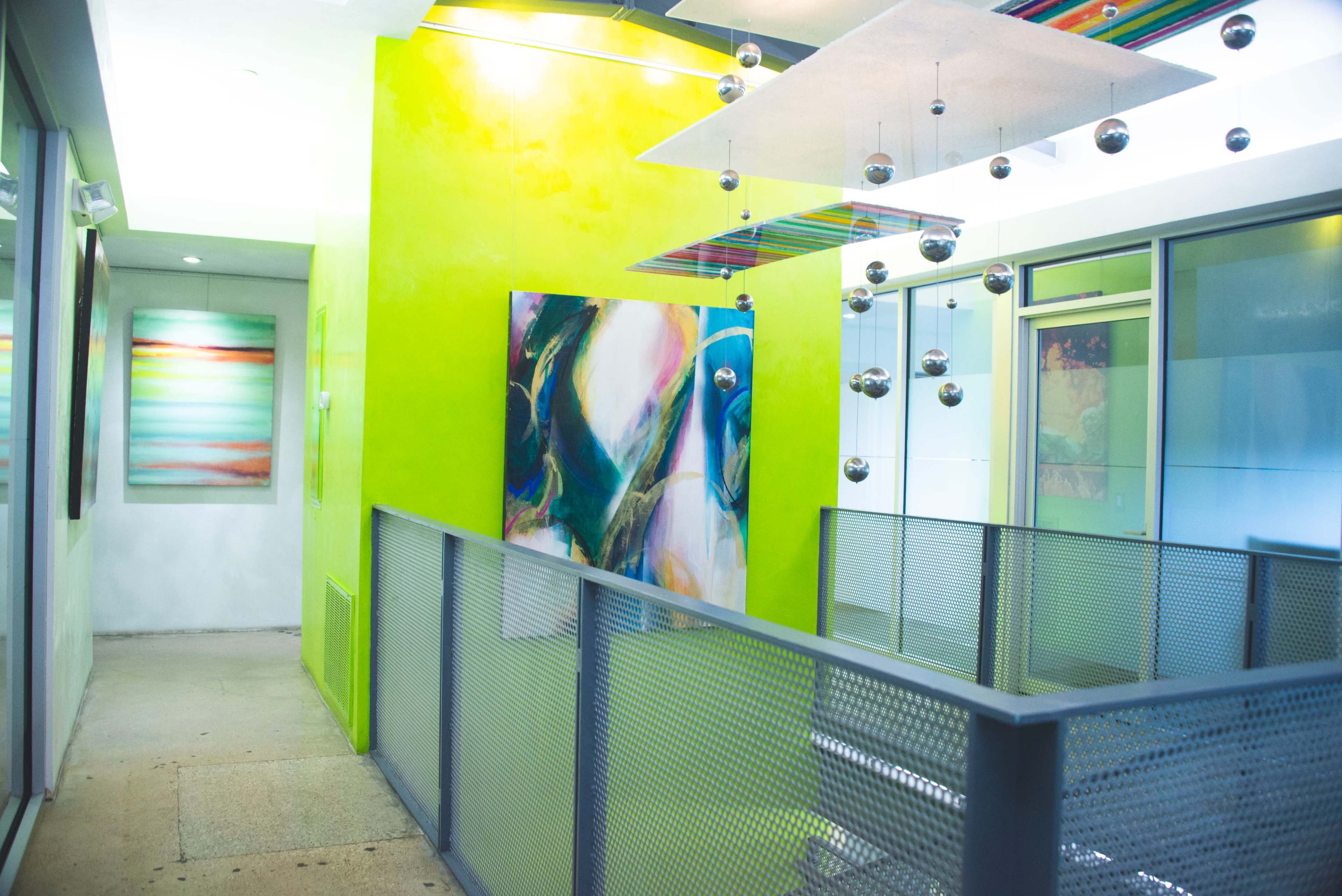 The image shows a brightly colored interior hallway with abstract artwork on the walls and metallic ornaments hanging from the ceiling.