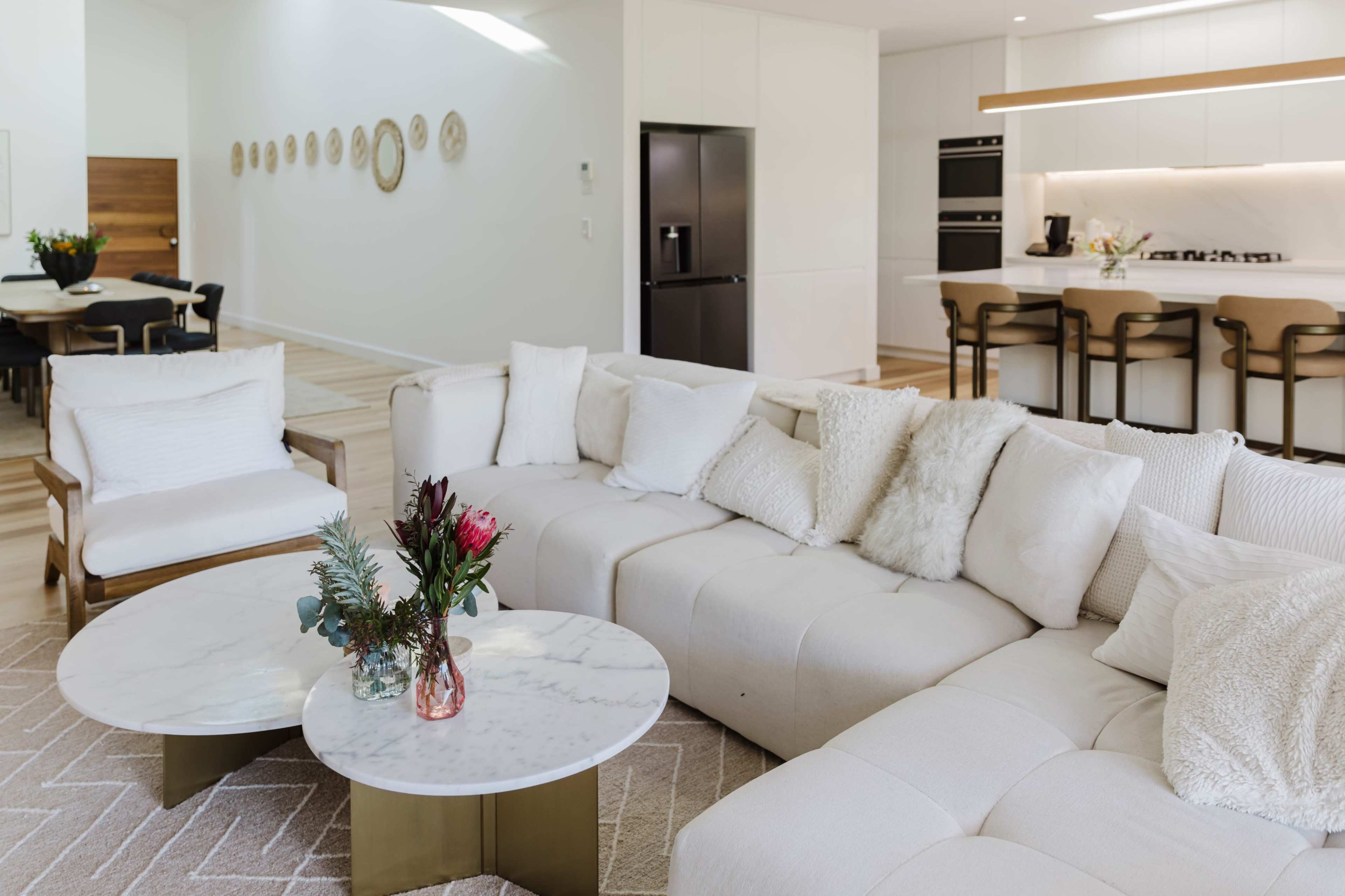 The image features a modern living room with a large white sectional sofa, a marble-topped coffee table, and a kitchen area visible in the background.