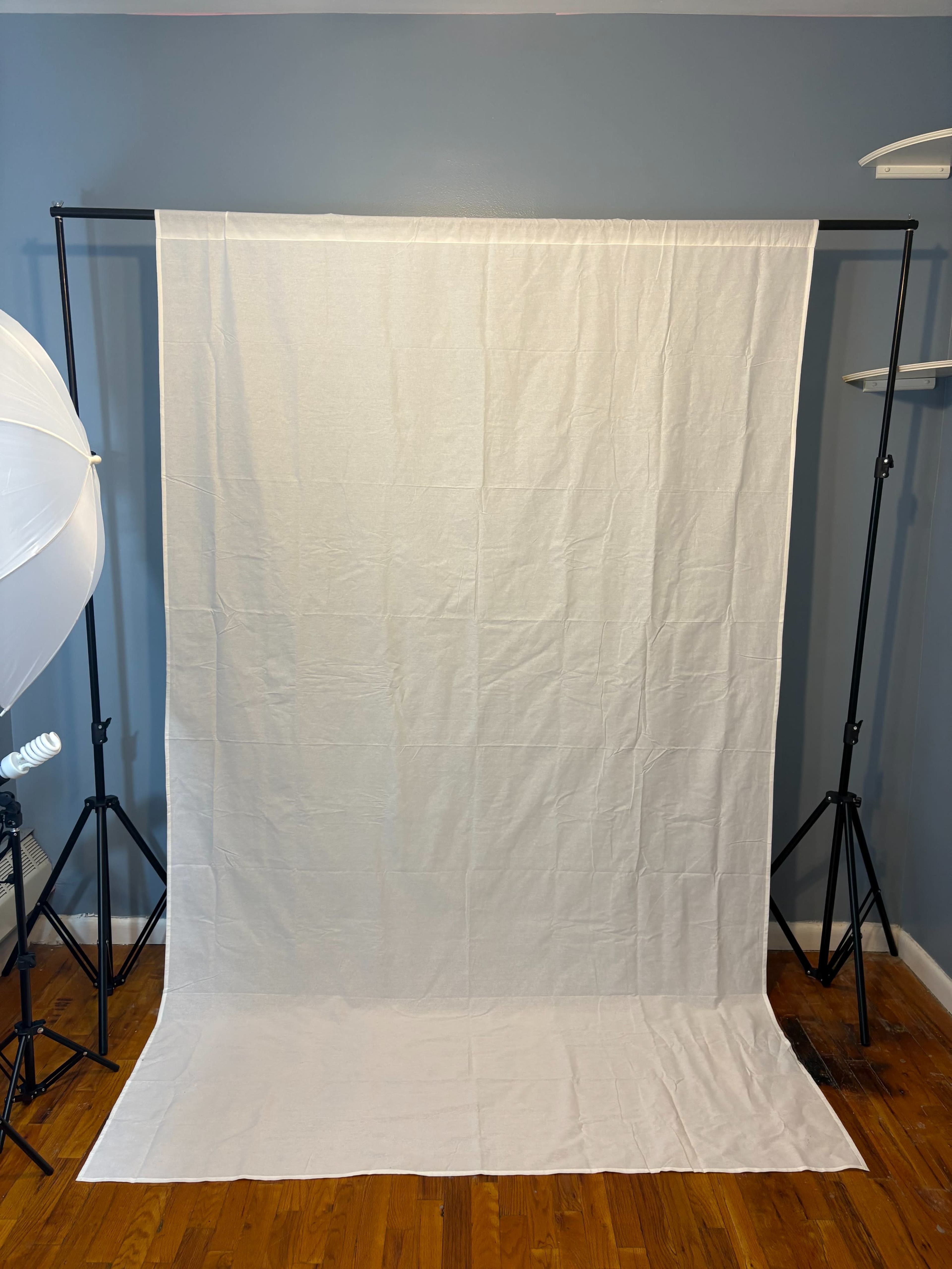 The image shows a plain white backdrop set up on a stand in a room with wooden flooring.