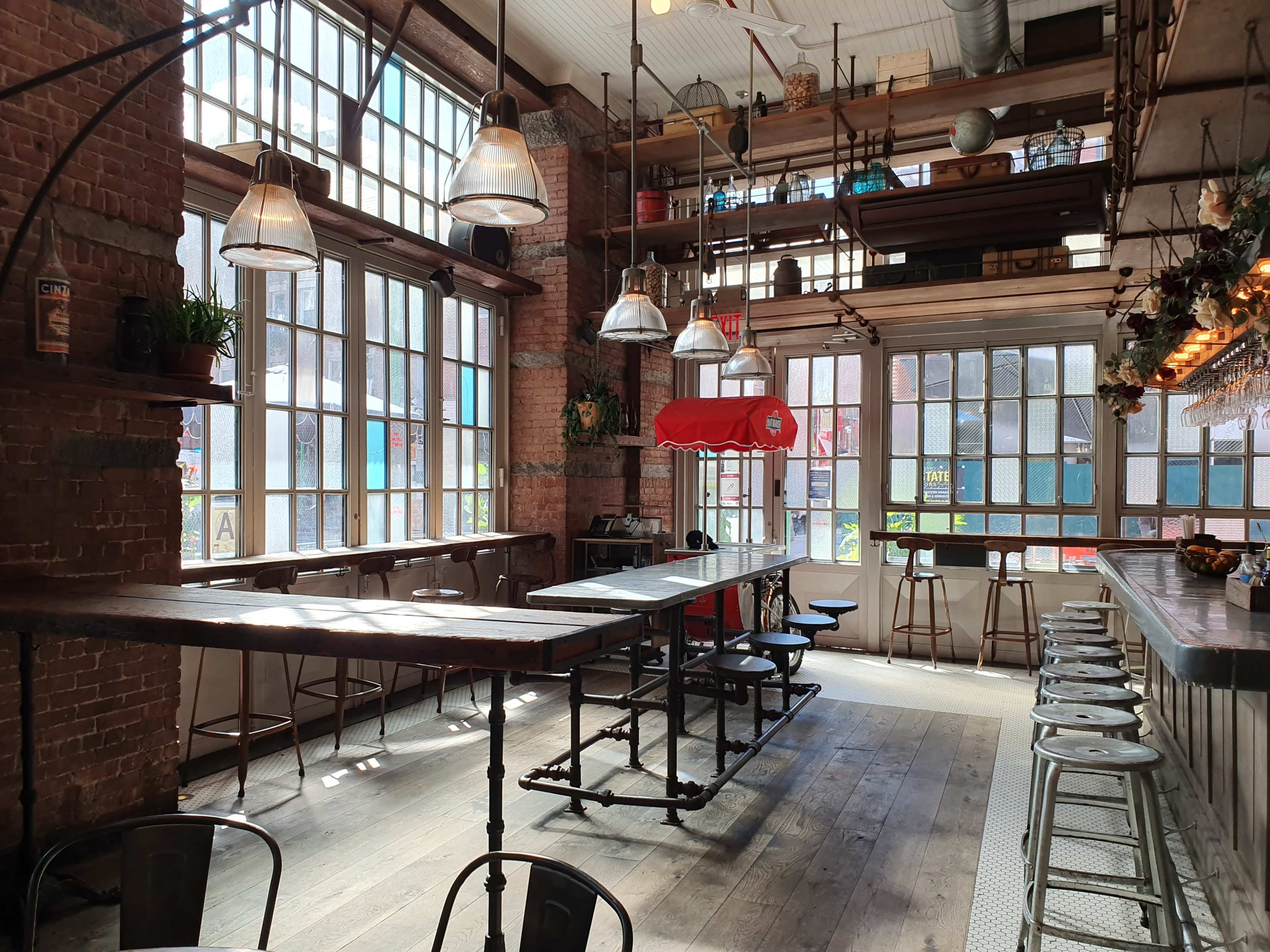 A spacious, industrial-style café with large windows, wooden flooring, and a long bar with stools.