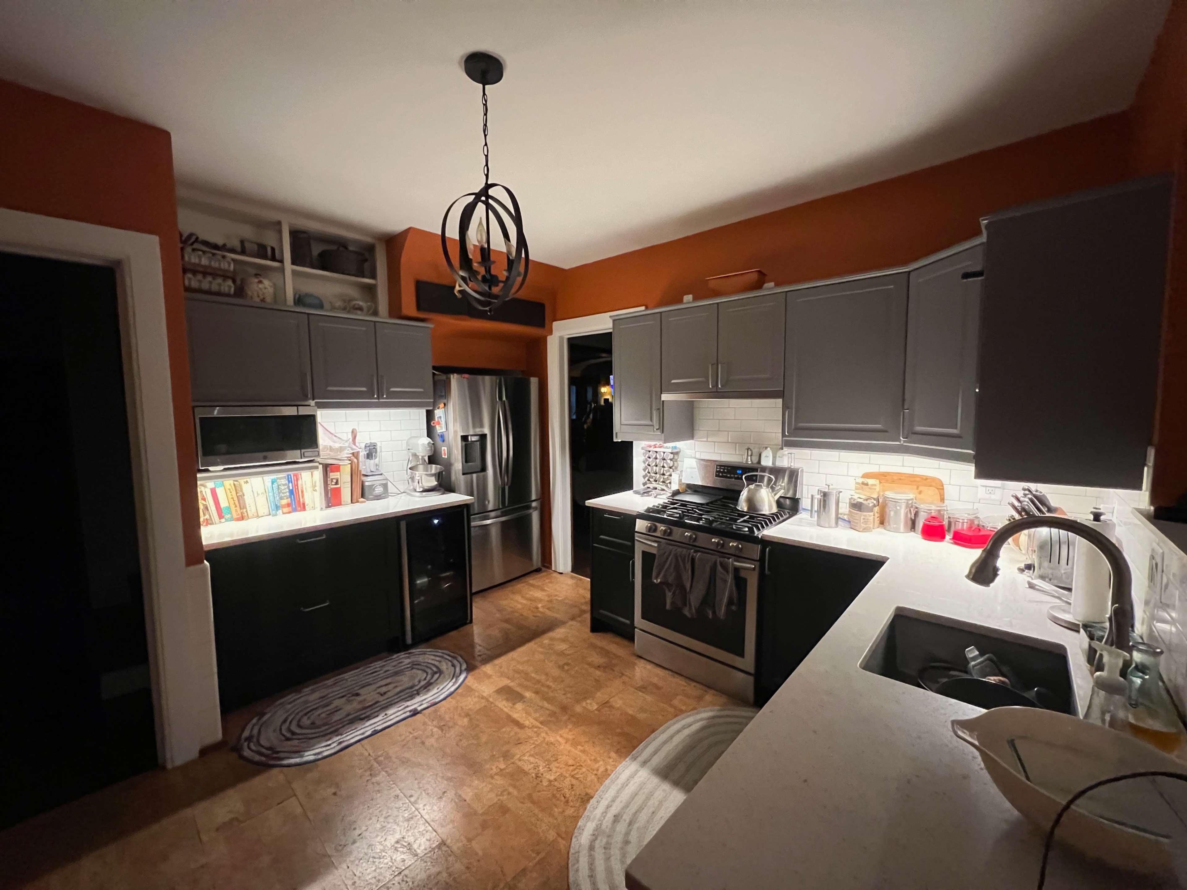 The kitchen features dark cabinets, a white countertop, and various appliances, with warm lighting illuminating the space.