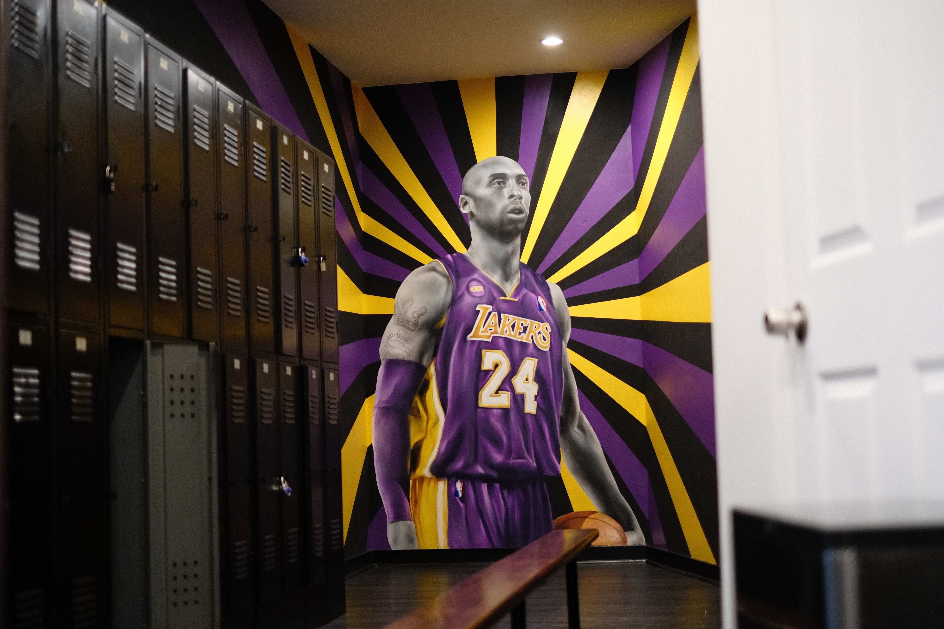 A mural of a basketball player in a purple and gold jersey in a hallway lined with metal lockers.