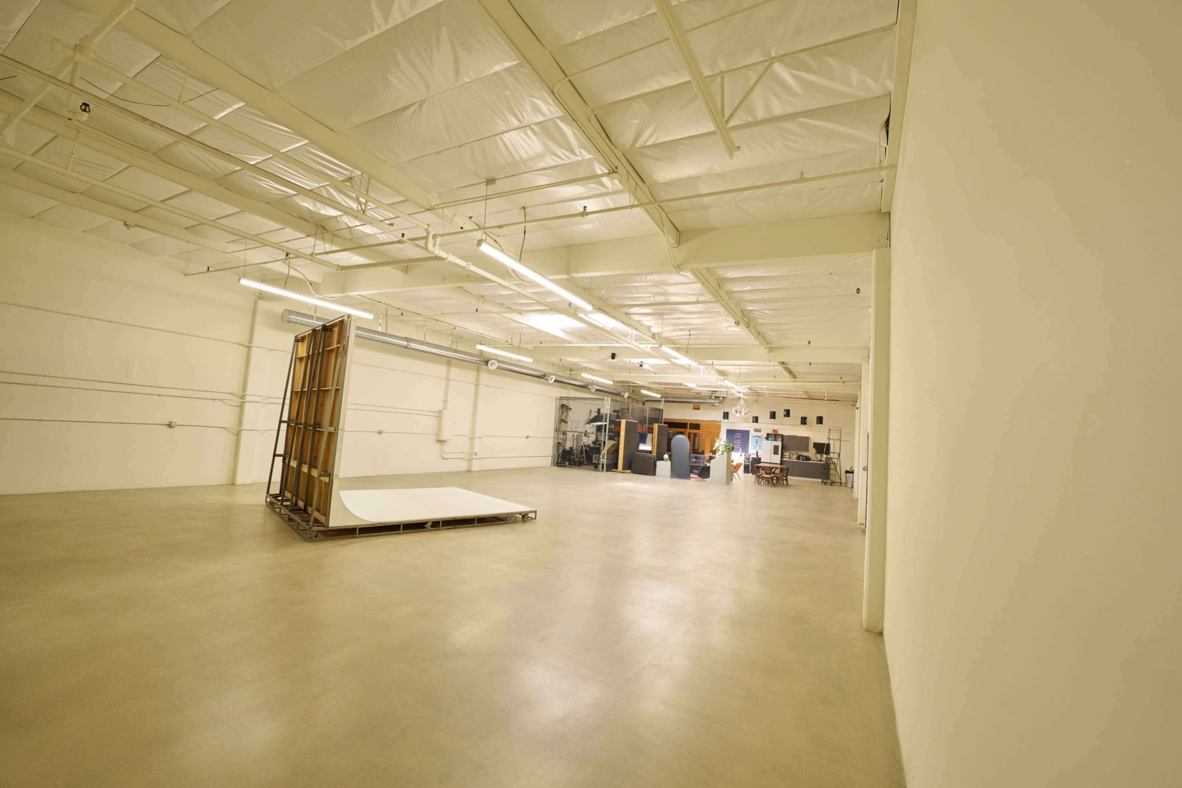 The image shows a large, empty industrial space with white walls, a concrete floor, and various equipment in the background.