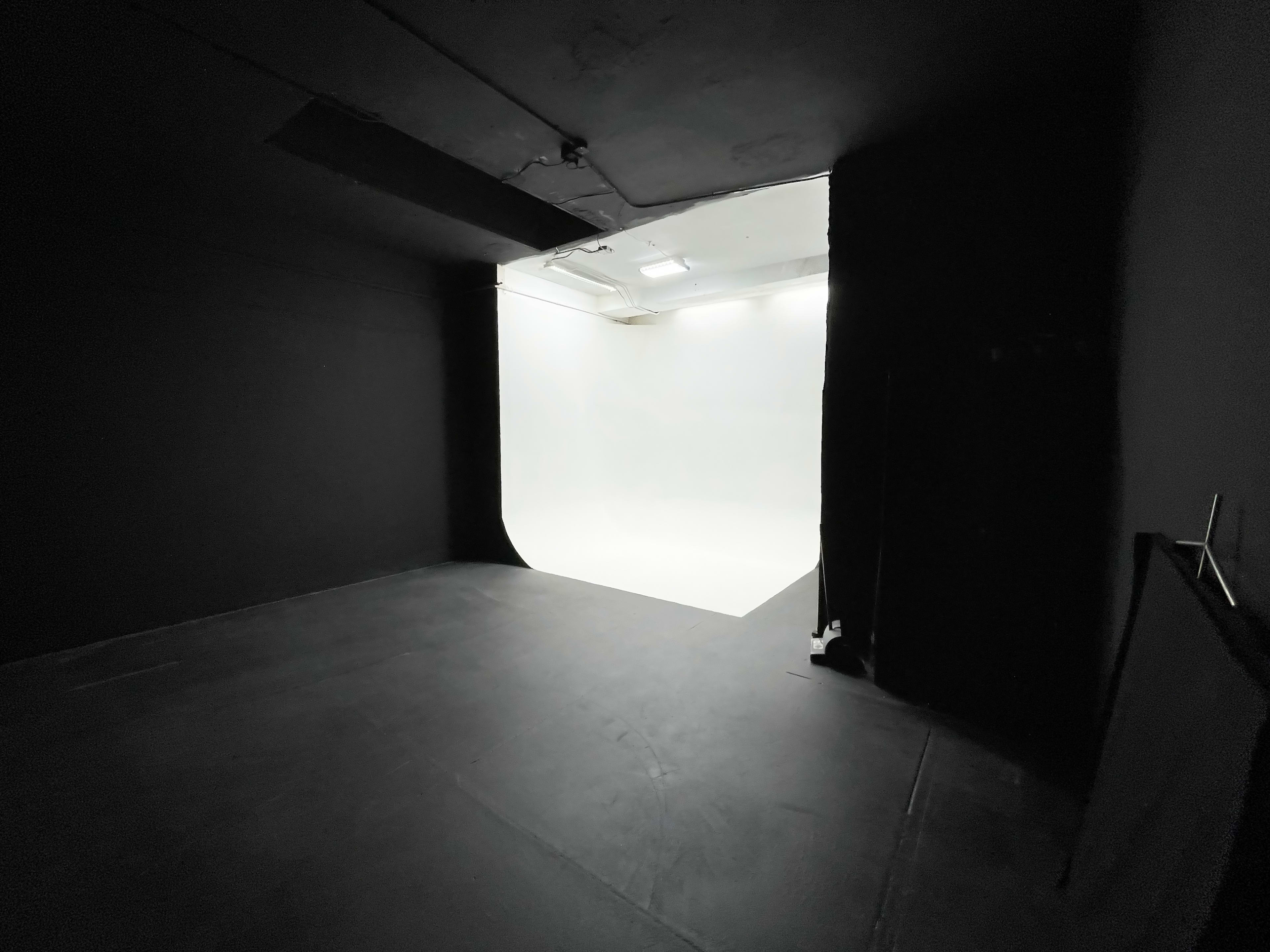 A dimly lit room with black walls and a white backdrop illuminated by overhead lights is visible.