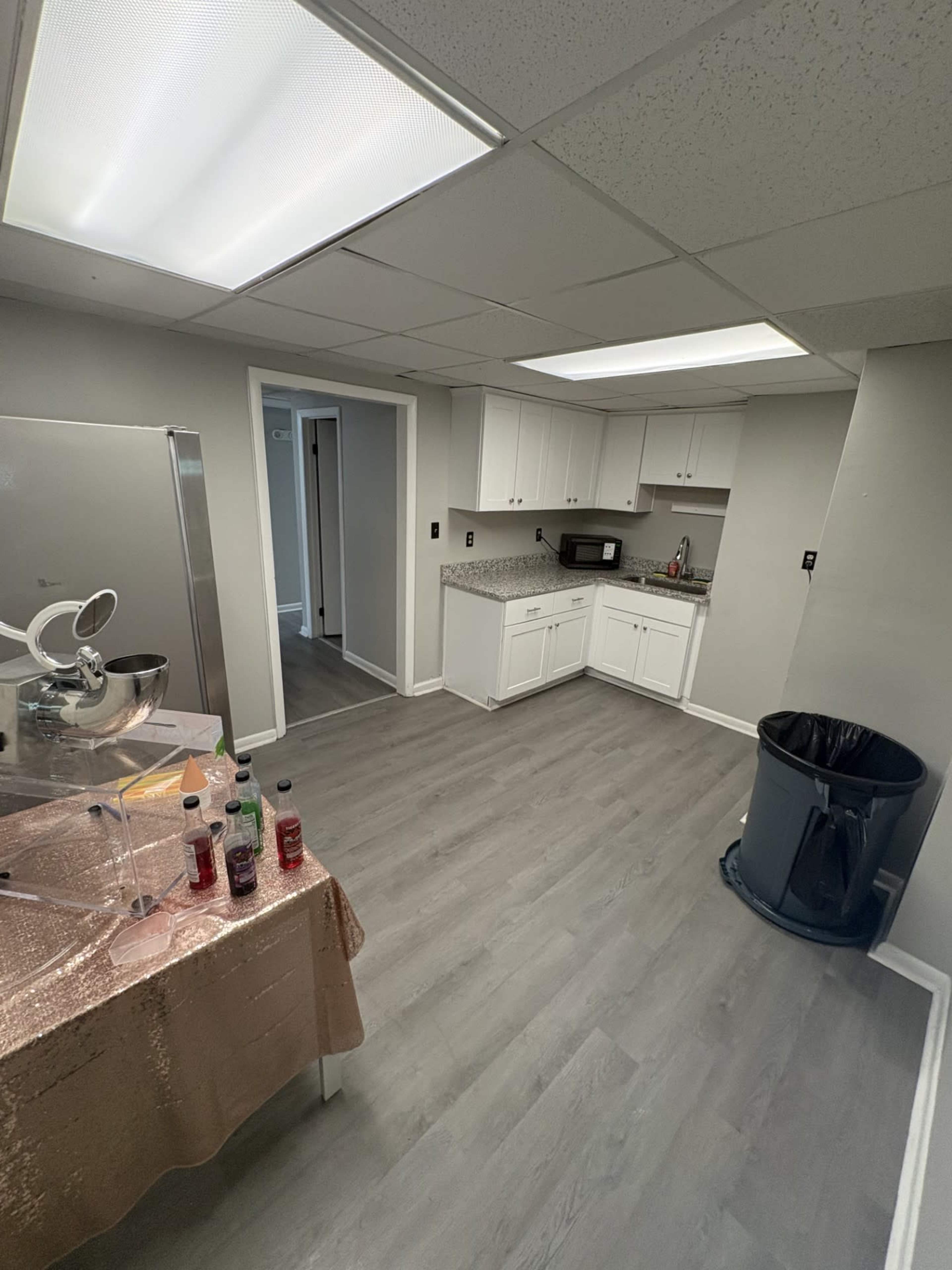 The image shows a modern kitchen with white cabinets, a countertop, a refrigerator, and a trash can, set on a light gray floor.