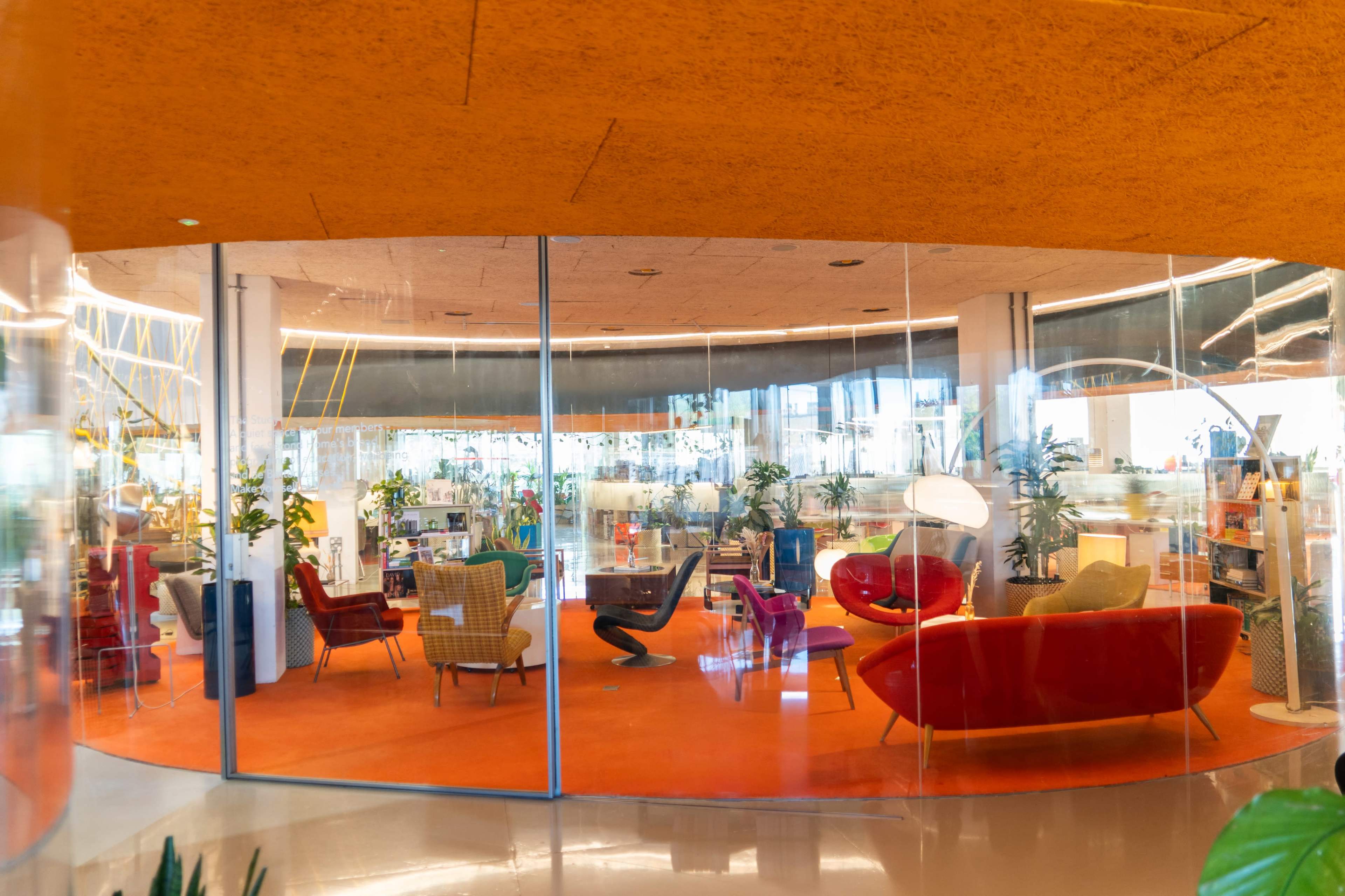 The image shows a modern office space featuring vibrant furniture, plants, and large glass walls.